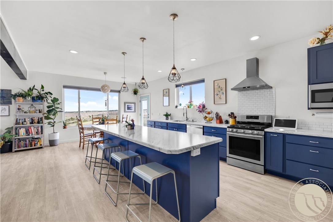 Kitchen with deep blue cabinets, a large white island, stainless steel appliances, and windows overlooking open land.