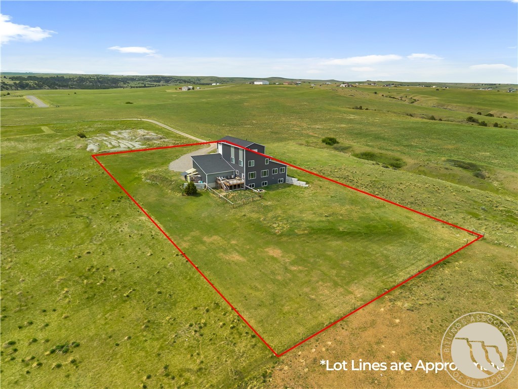 Aerial view of a multi-level house on a large grassy lot outlined in red, surrounded by rolling fields.