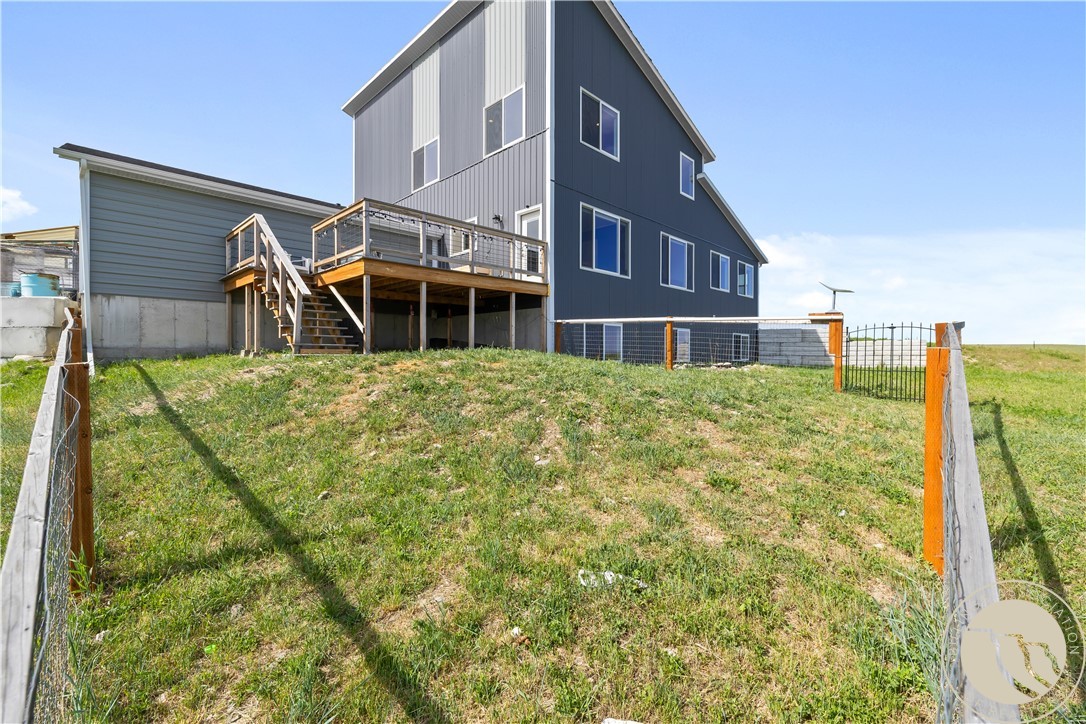 Dark-sided house with a raised wooden deck and stairs behind a fenced grassy yard.