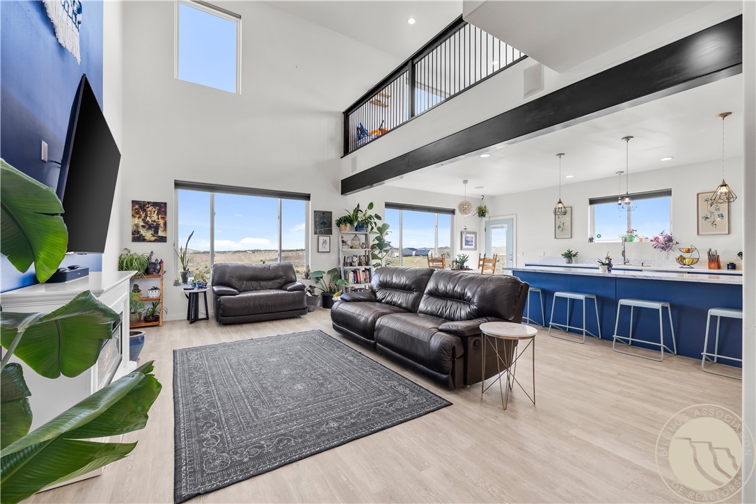 Living room with black leather sofas, a patterned rug, vaulted ceiling, and long blue kitchen island.