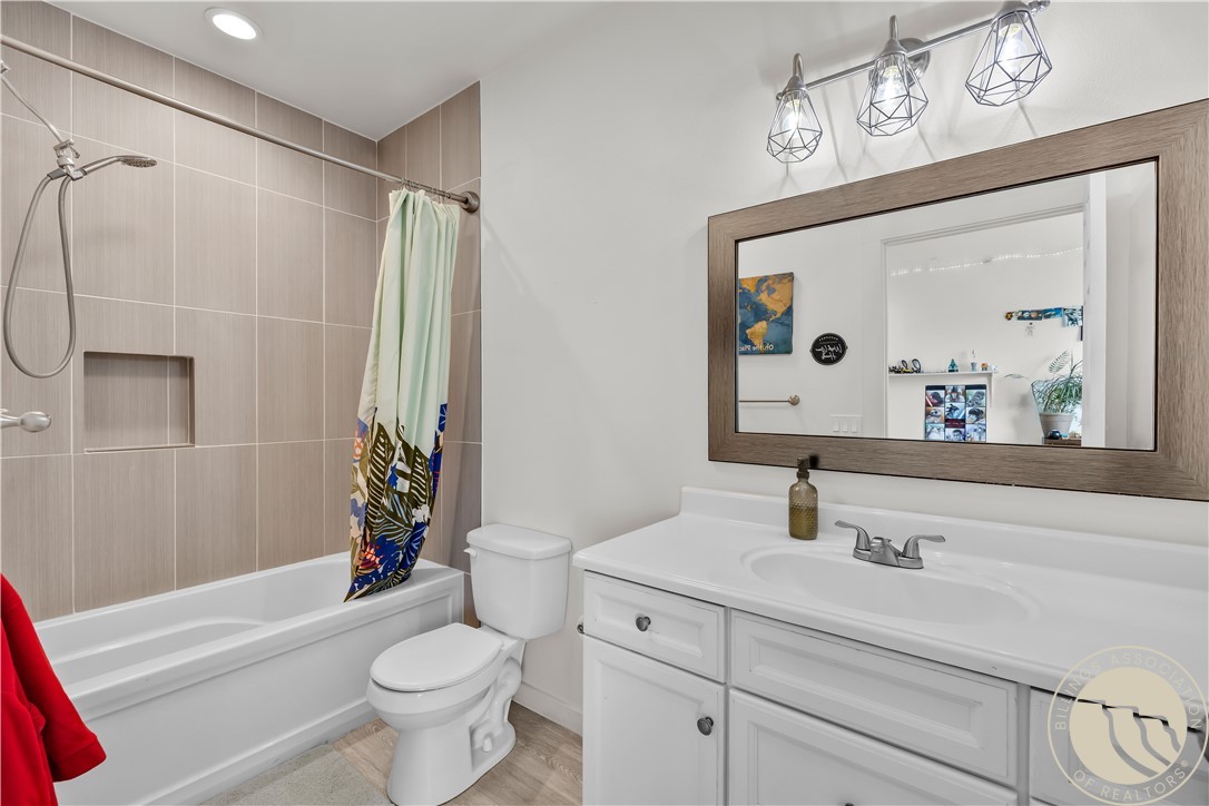 Bathroom with a taupe-tiled tub and shower, white vanity, and large wood-framed mirror.