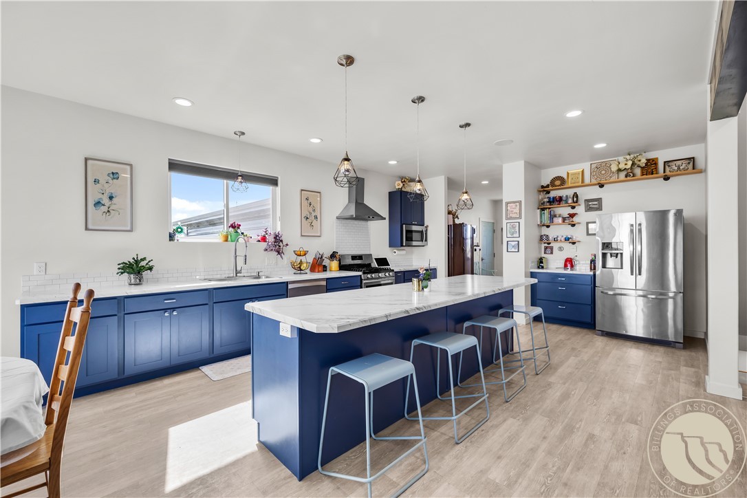 Kitchen with blue cabinets, a large island with stools, and stainless steel appliances.