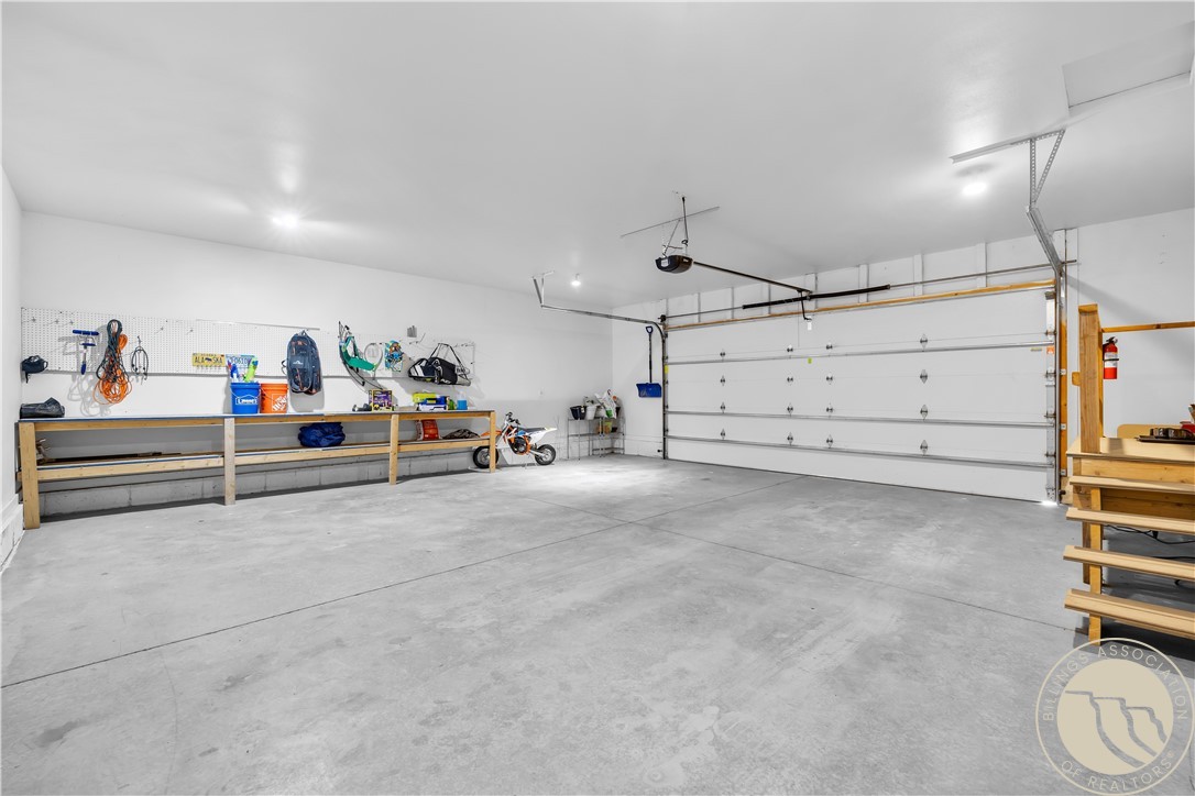 Spacious garage with a large overhead door, concrete floor, tool-lined workbench, and a small motorcycle.