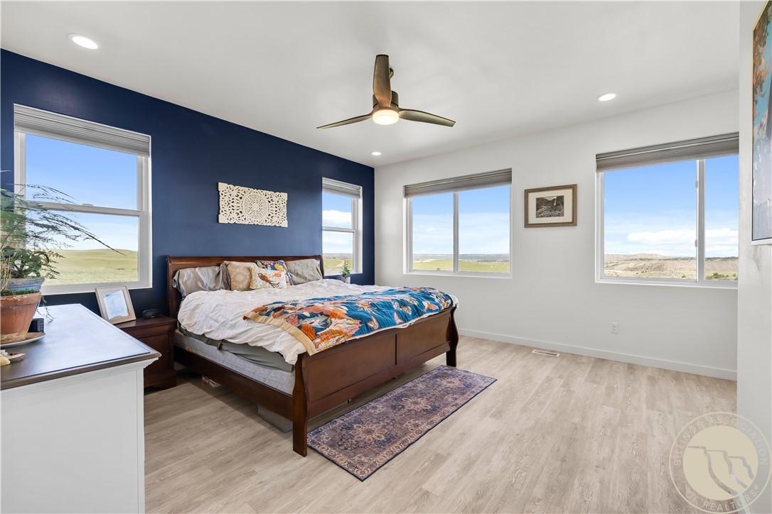 Bedroom with a dark wood bed and colorful quilt beside large windows overlooking open countryside.