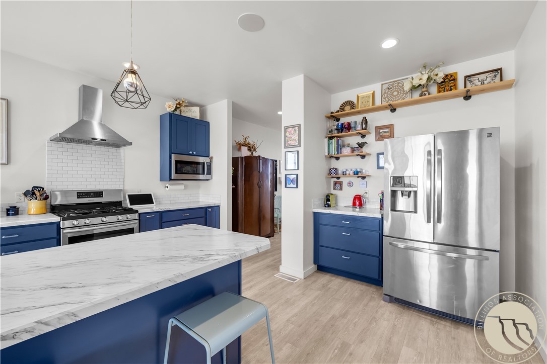 Kitchen with blue cabinetry, a large marble-look island, and stainless steel appliances.