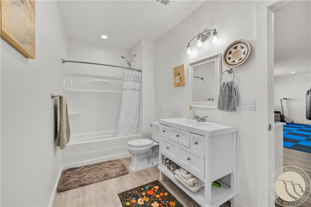 Bathroom with a white bathtub, toilet, and vanity; doorway opens to a room with blue-and-black flooring.