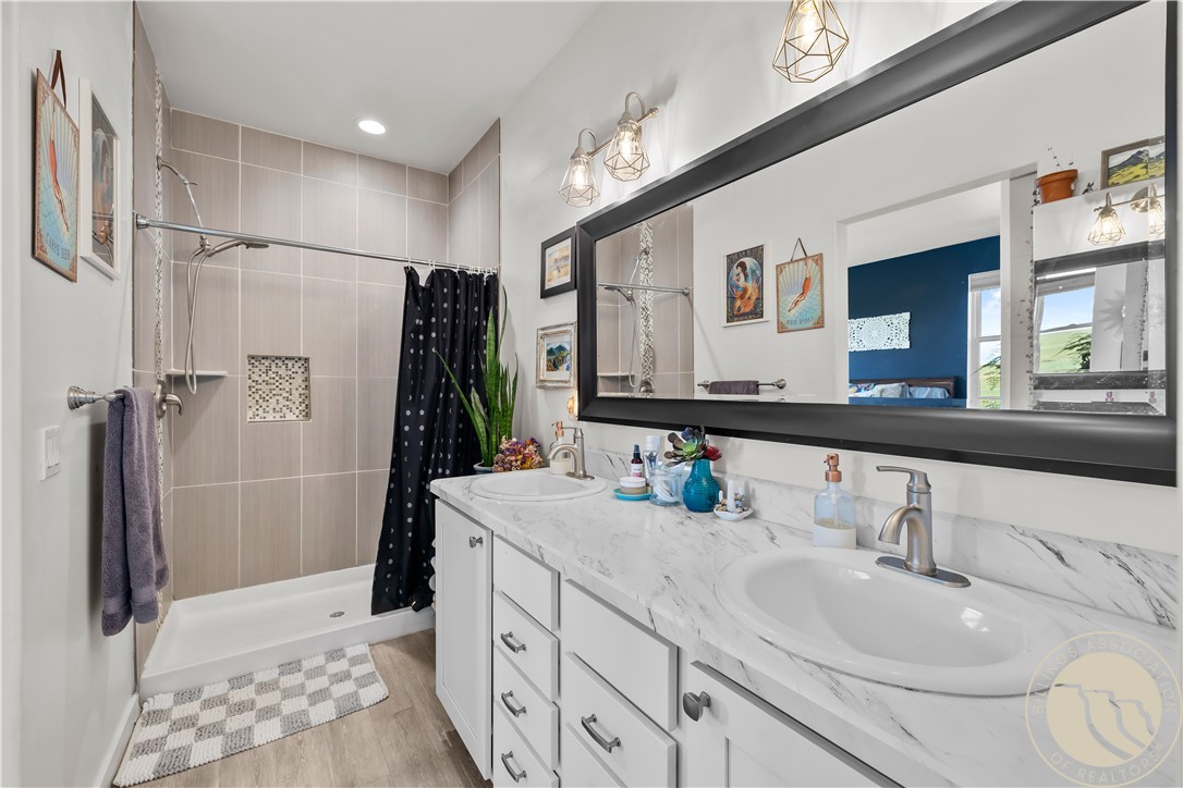Bathroom with a double-sink vanity, marble-look countertop, and tiled shower with a dark curtain.