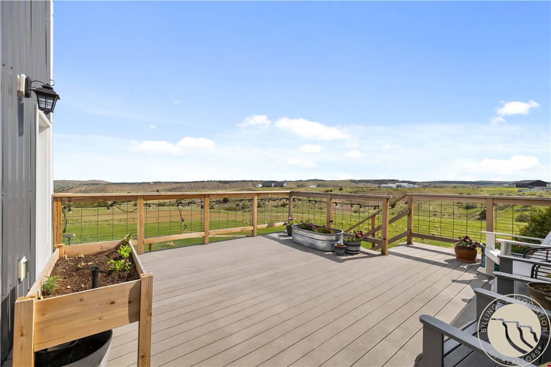 Spacious deck with raised planters and cable railings overlooking open fields and distant hills.