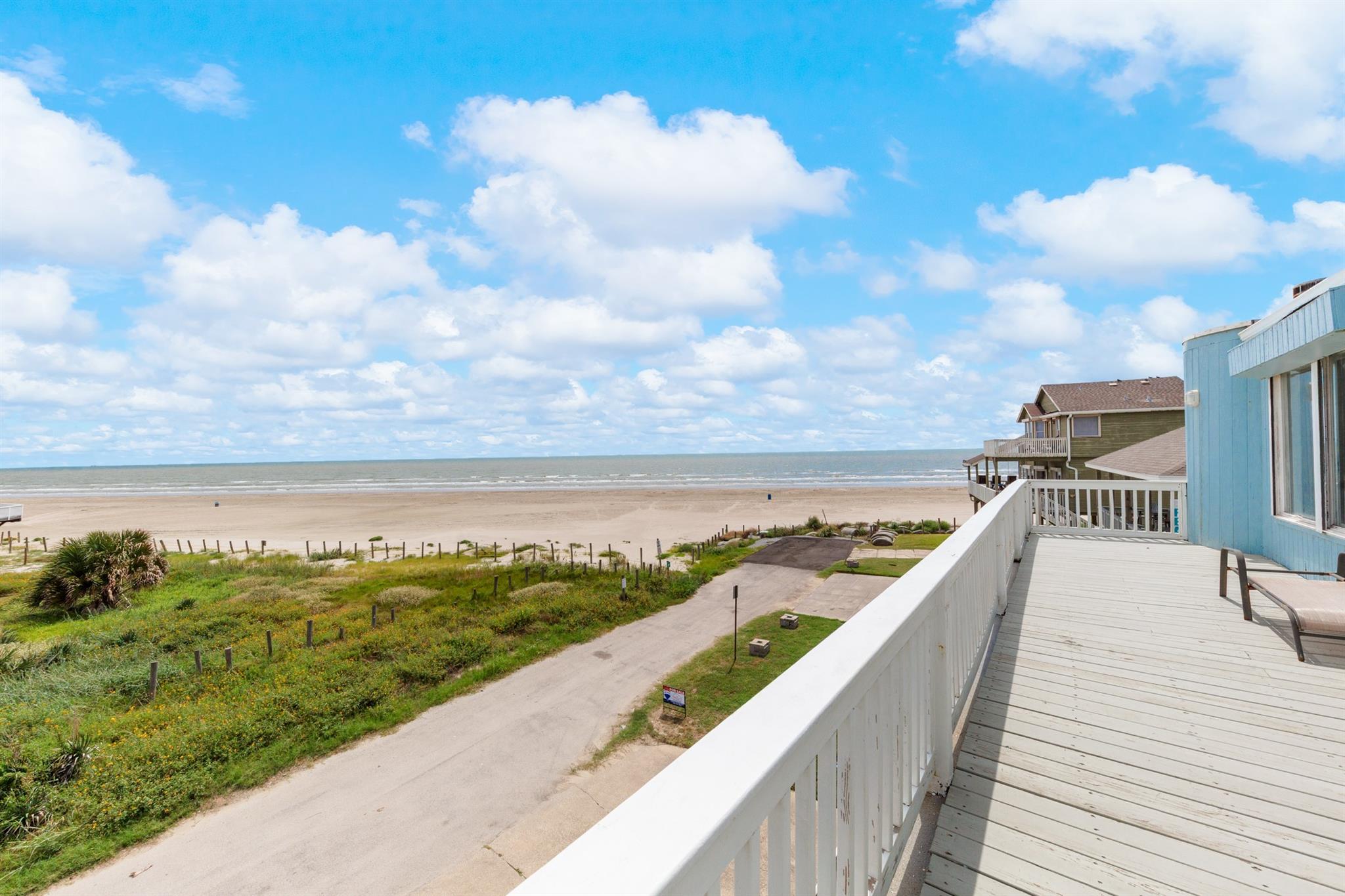 Coastal deck overlooking beach and ocean, with beach houses along the shore.
