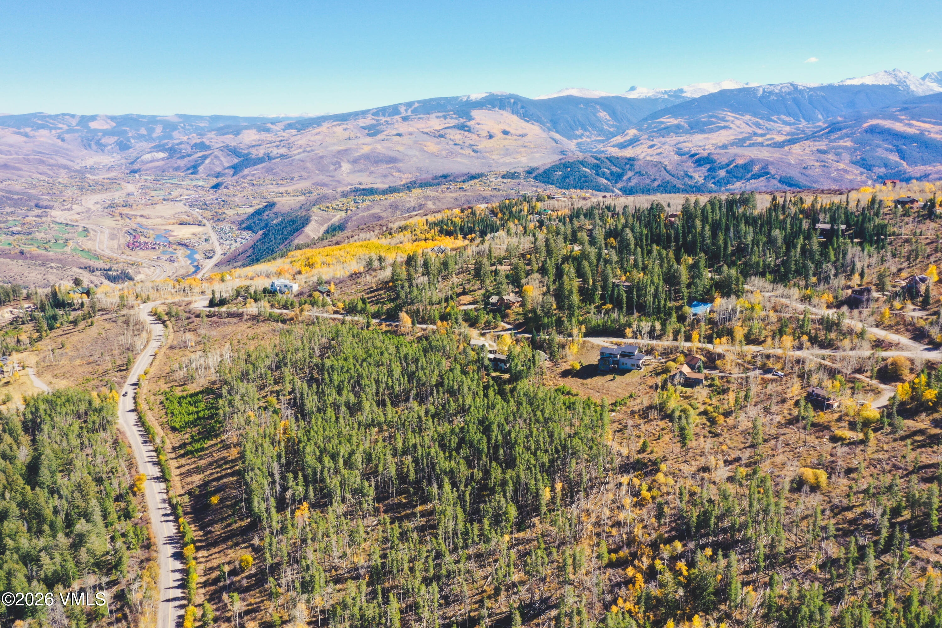Wooded hillside lot with scattered homes, a winding road, and distant snow-capped mountains.