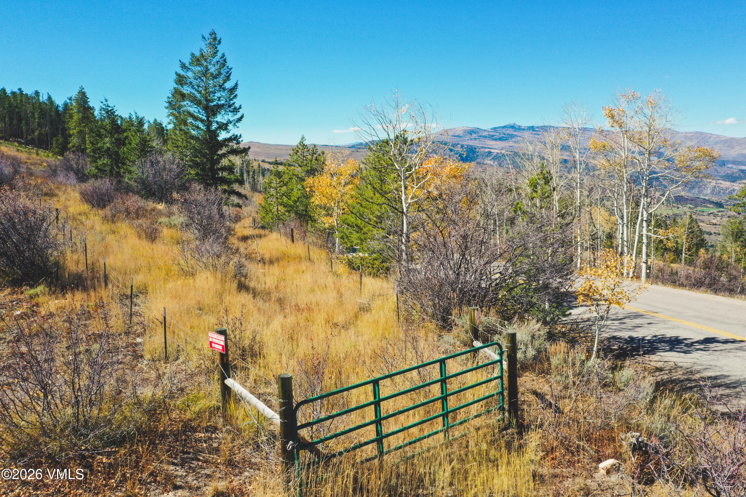 Grassy vacant lot with a green gate, roadside access, and distant mountain views.