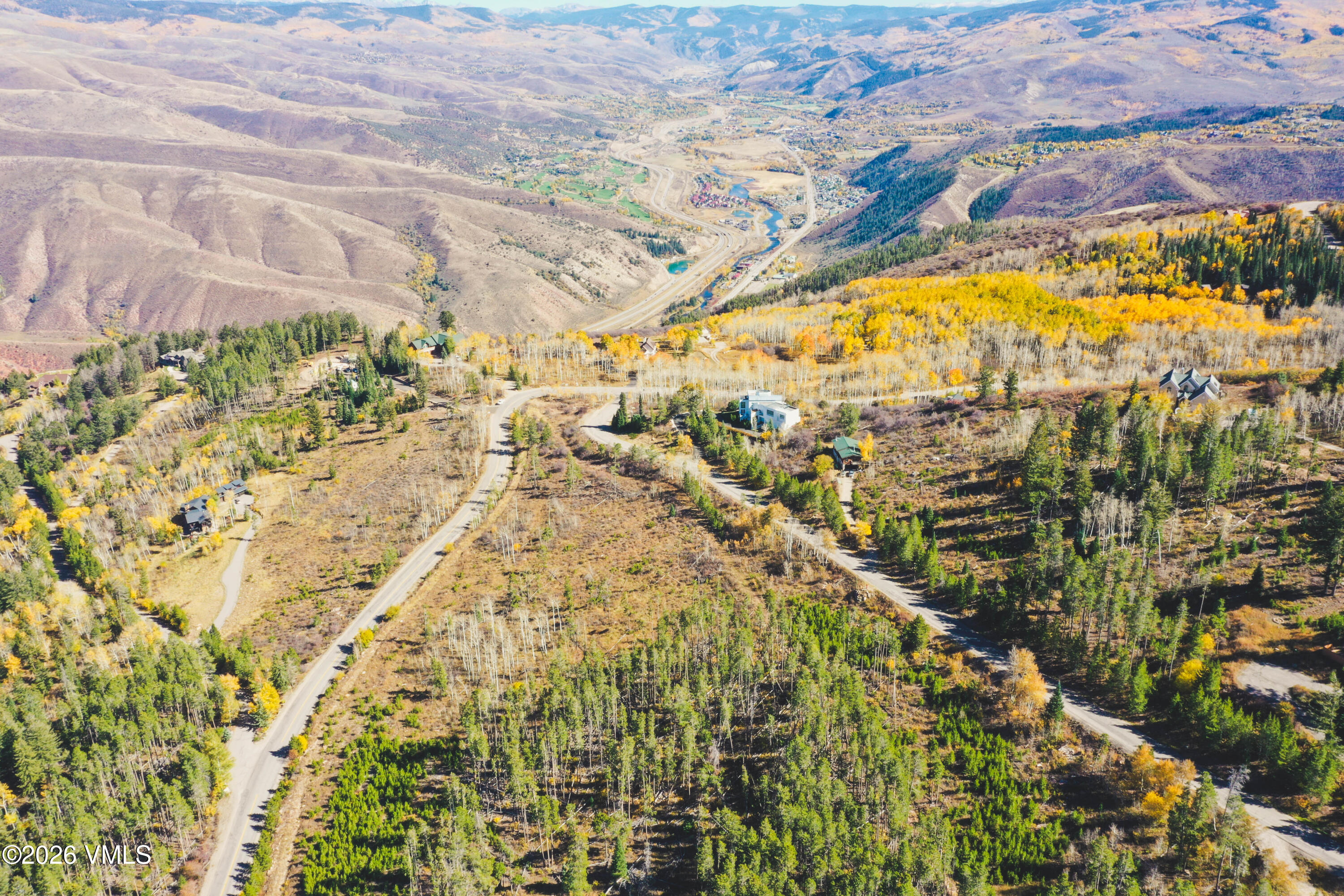 Aerial view of a wooded lot with winding roads, golden aspens, and mountain valleys beyond.