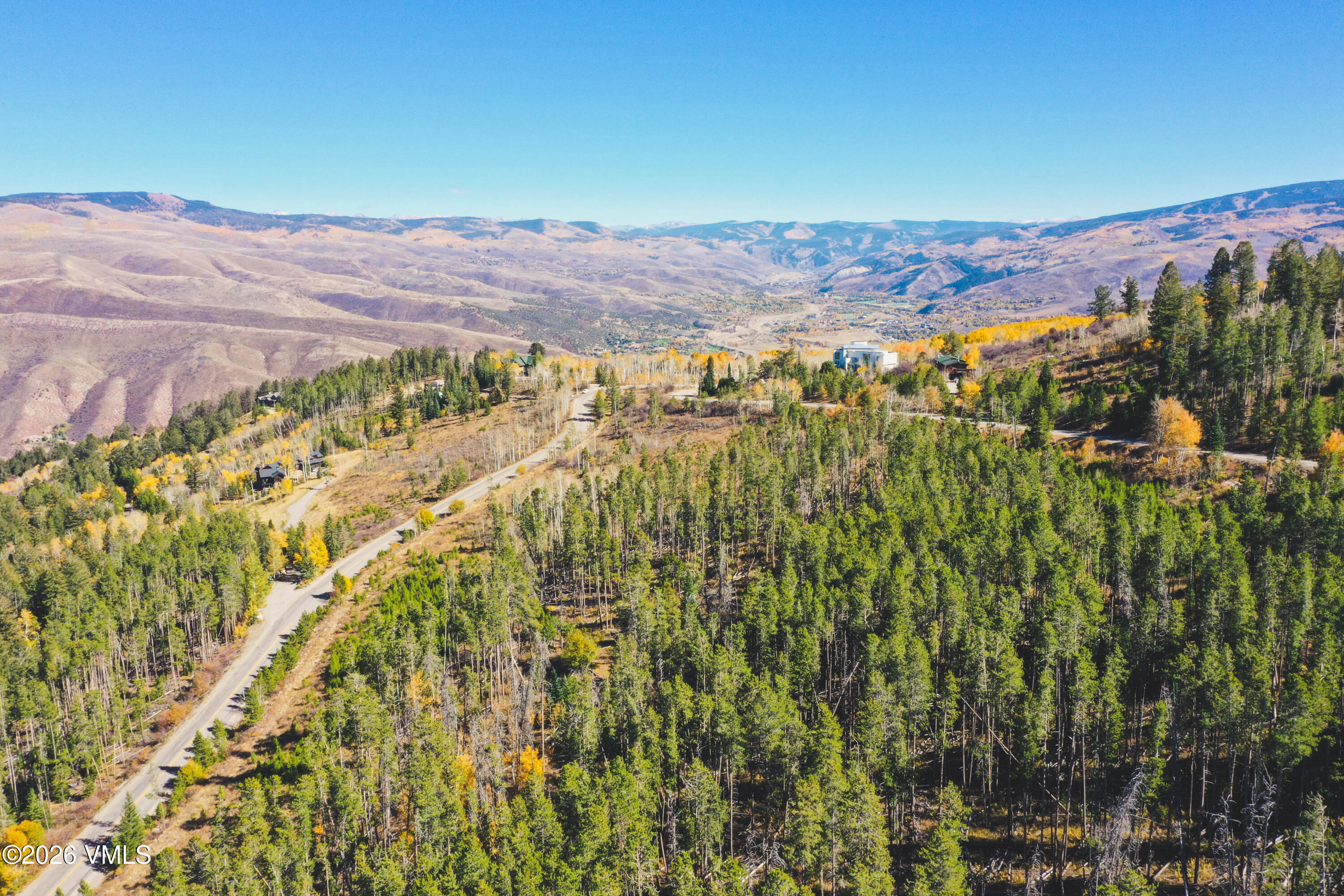 Aerial view of a forested ridge with a winding road, golden aspens, and a wide mountain valley.