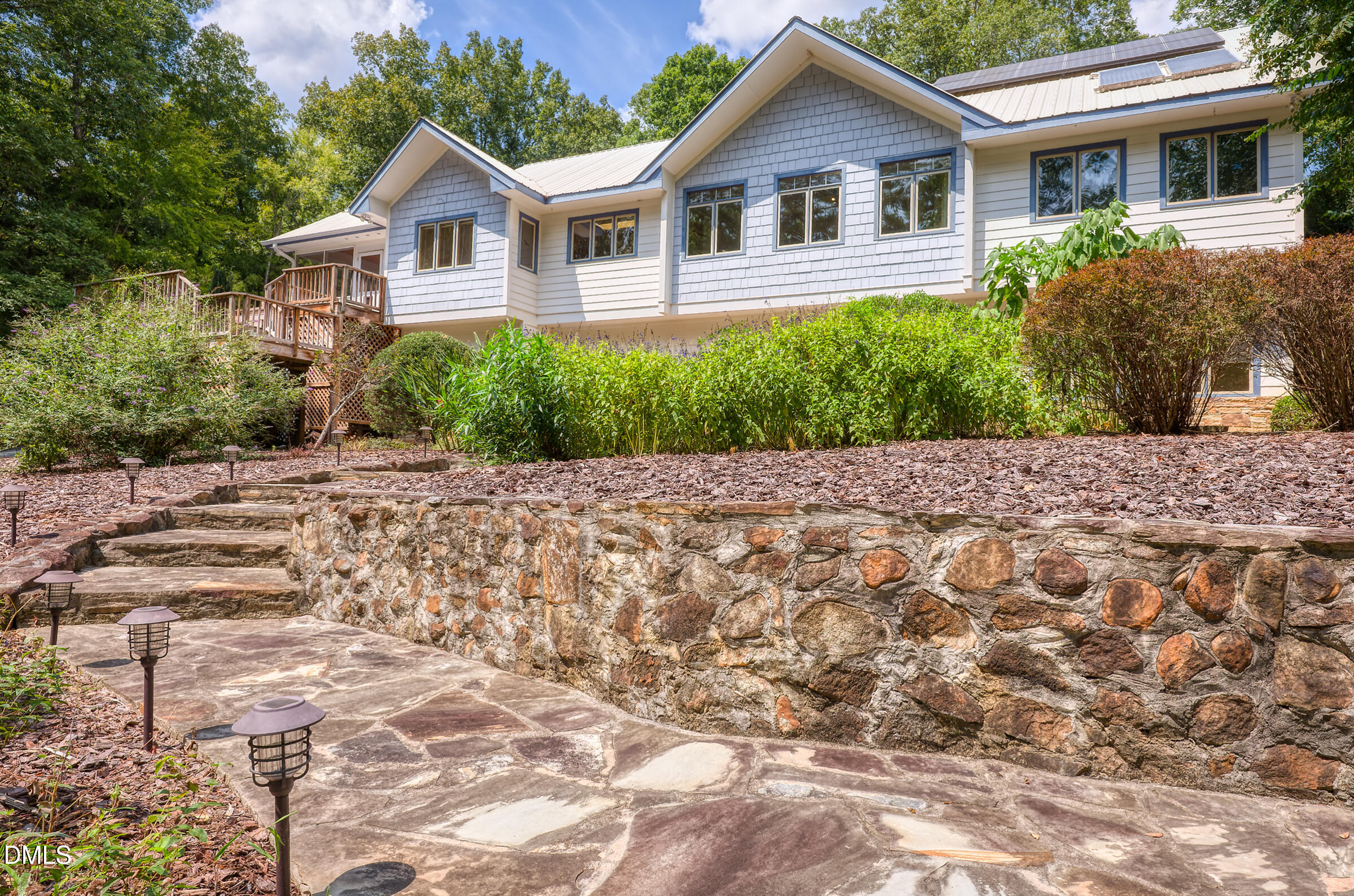 White gabled home above a stone retaining wall, with a wooden deck and flagstone walkway.