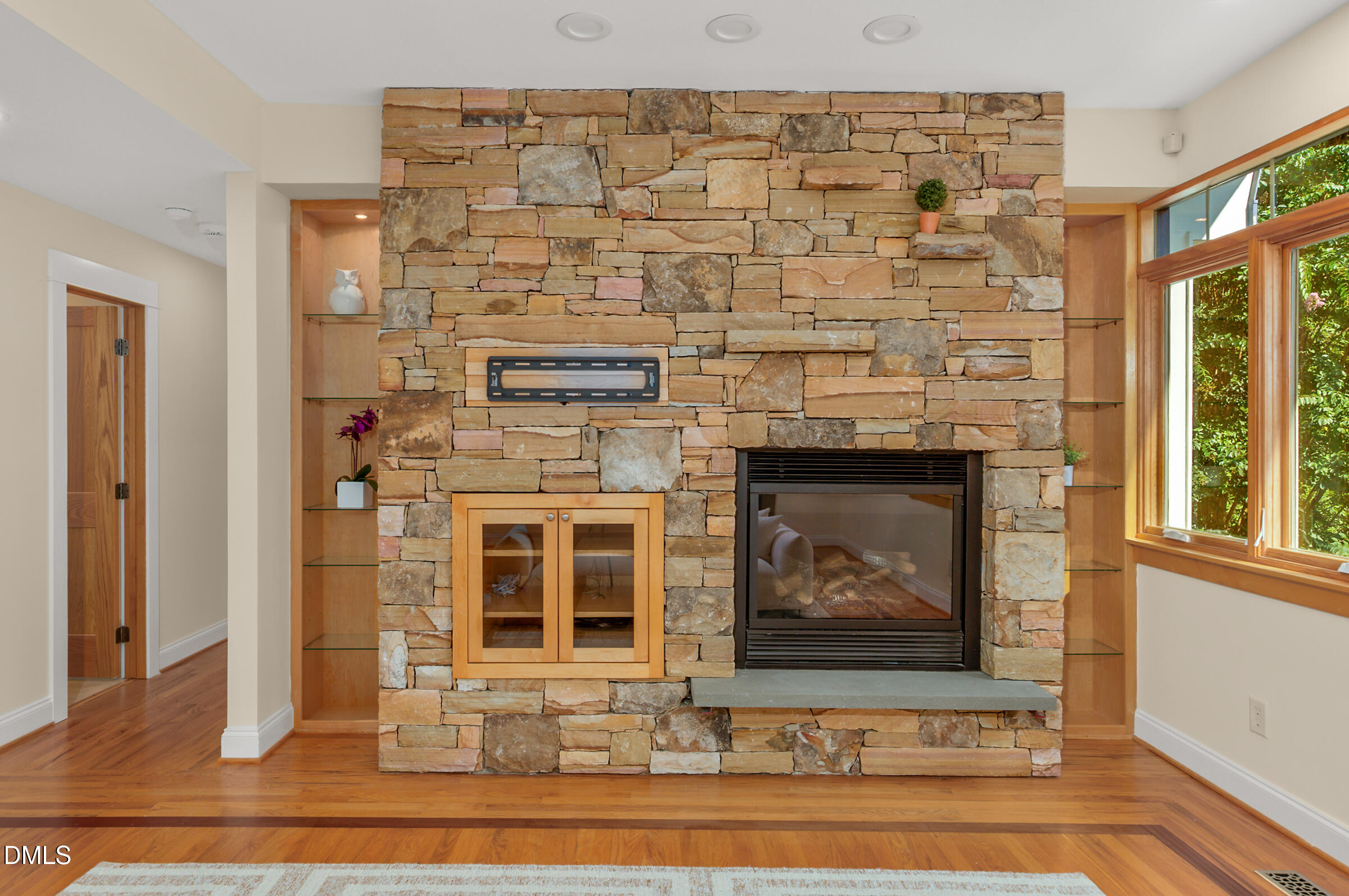 Living room with a floor-to-ceiling stone fireplace, built-in shelves, hardwood floors, and large windows.