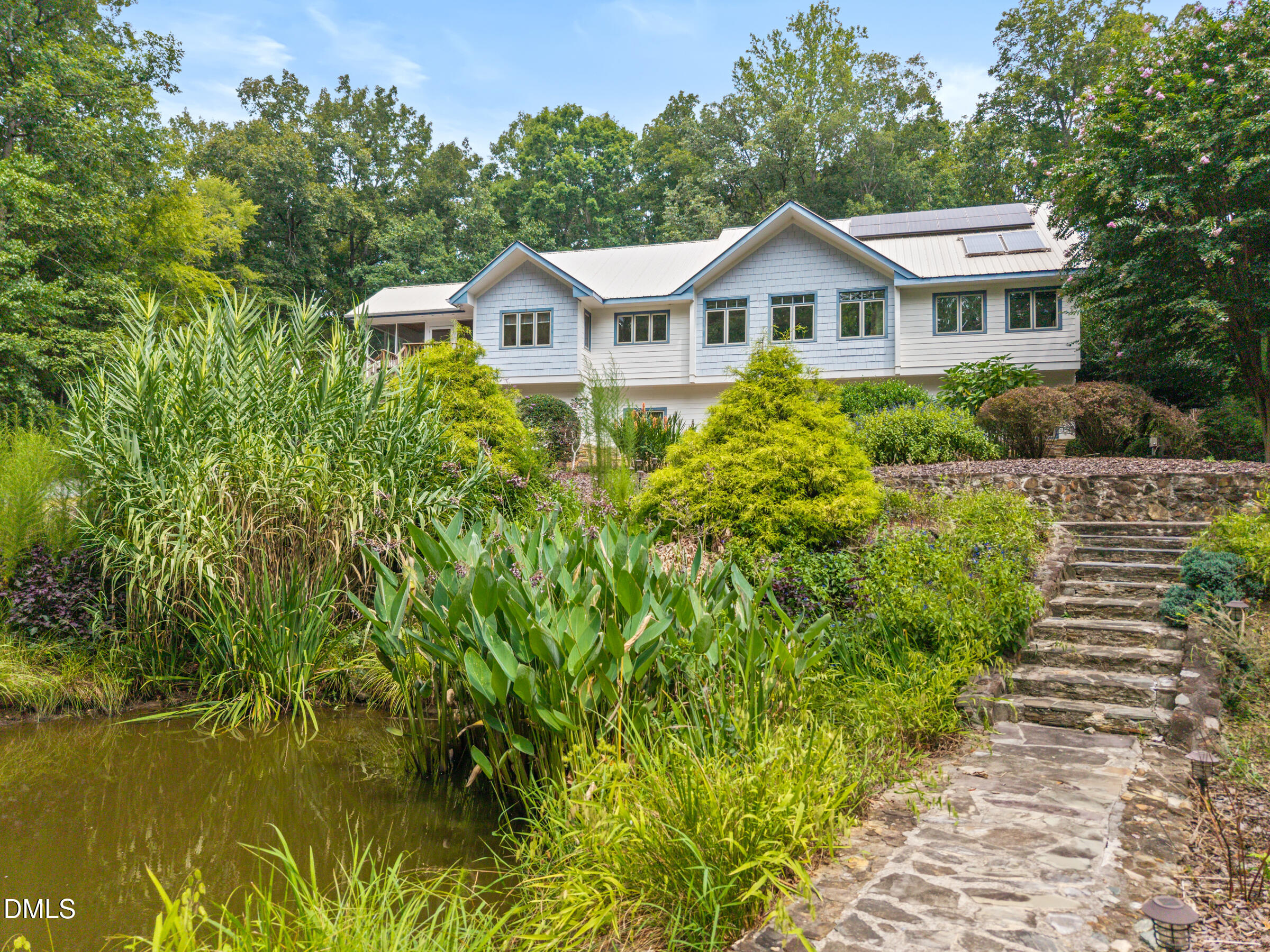 White home with rooftop solar panels above a landscaped pond and stone steps.