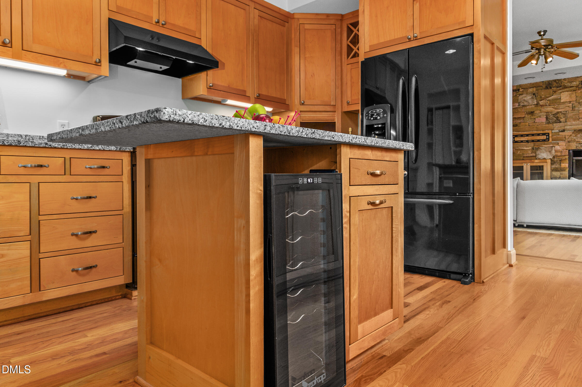 Kitchen with wood cabinets, granite island, black appliances, and a wine cooler.