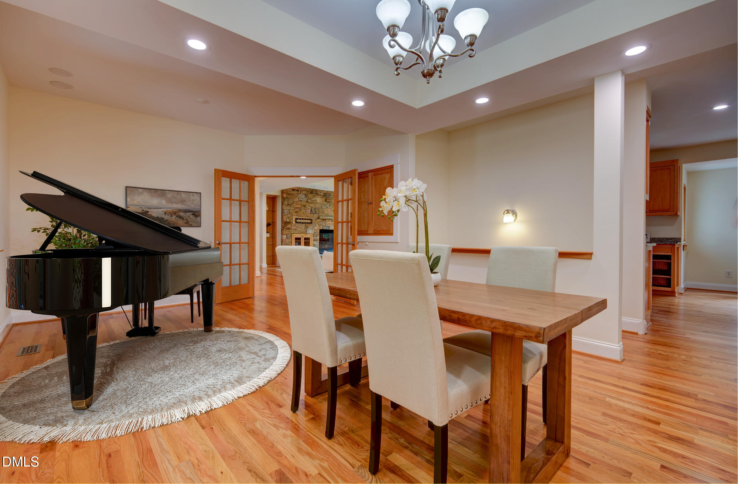 Dining room with a grand piano, wooden table, hardwood floors, and open doors to a stone fireplace.