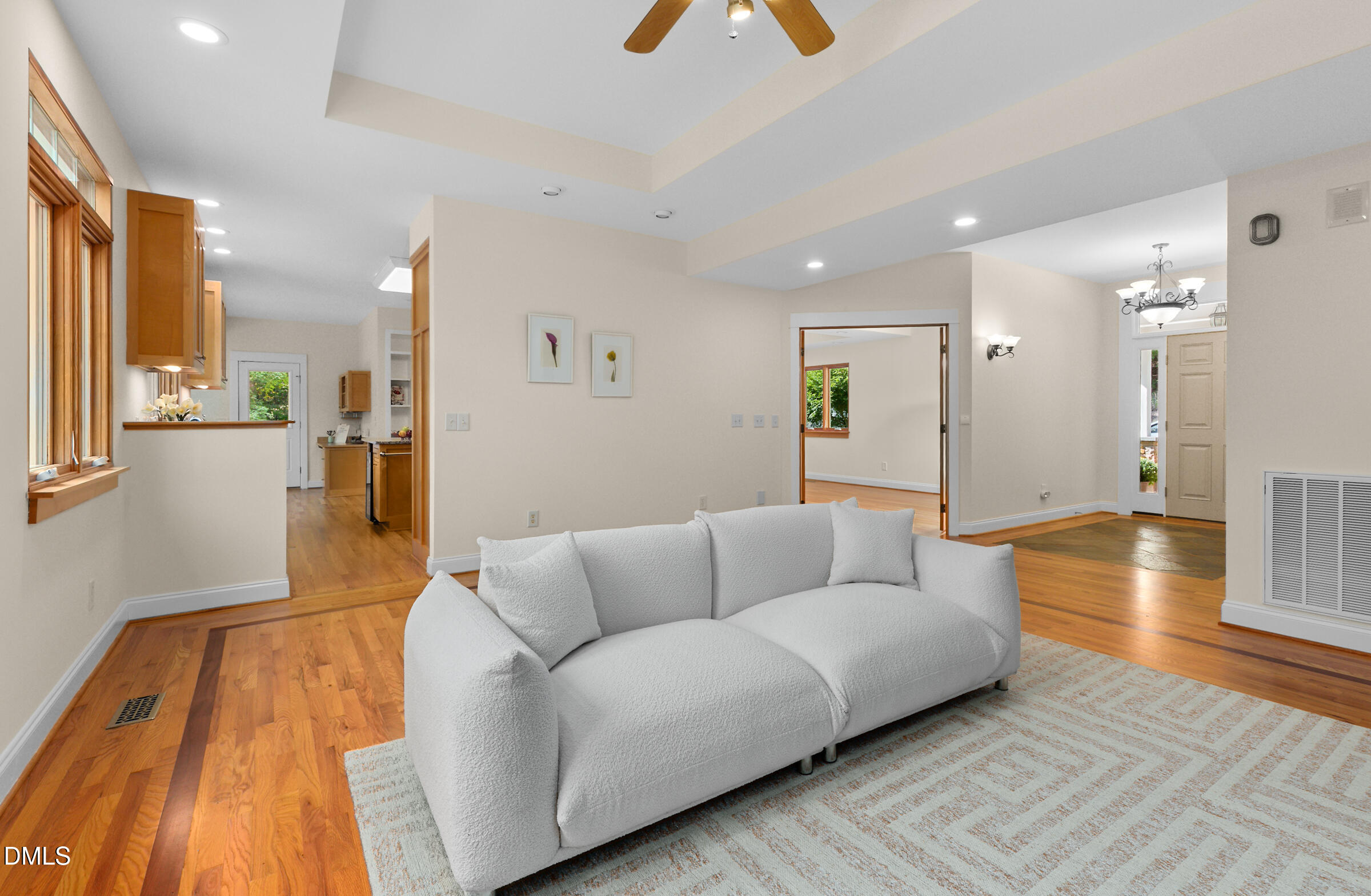 Open-plan living room with a white sofa, warm hardwood floors, and a tray ceiling.