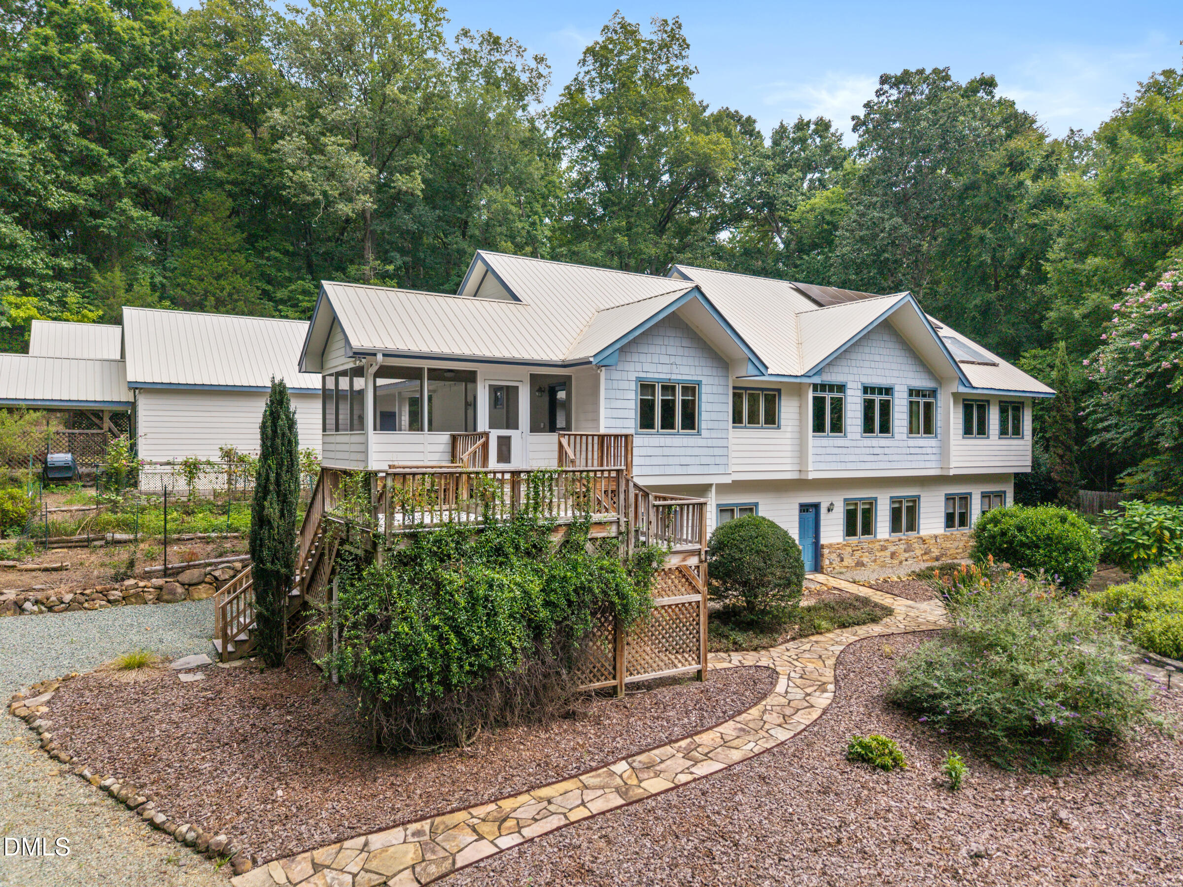 White multi-level home with a metal roof, raised wooden deck, and curved stone walkway.