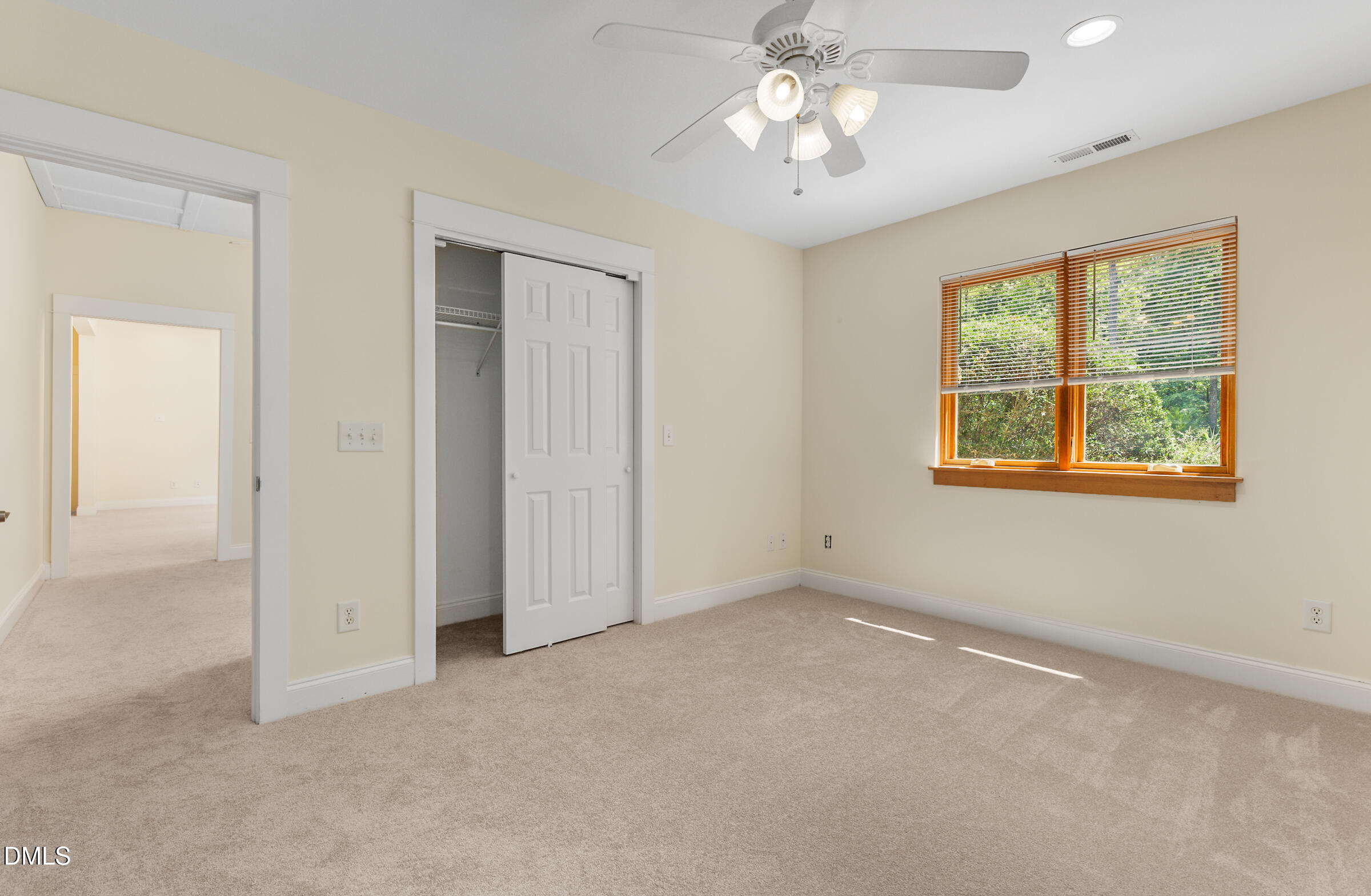 Unfurnished bedroom with beige carpet, a ceiling fan, and a window overlooking greenery.