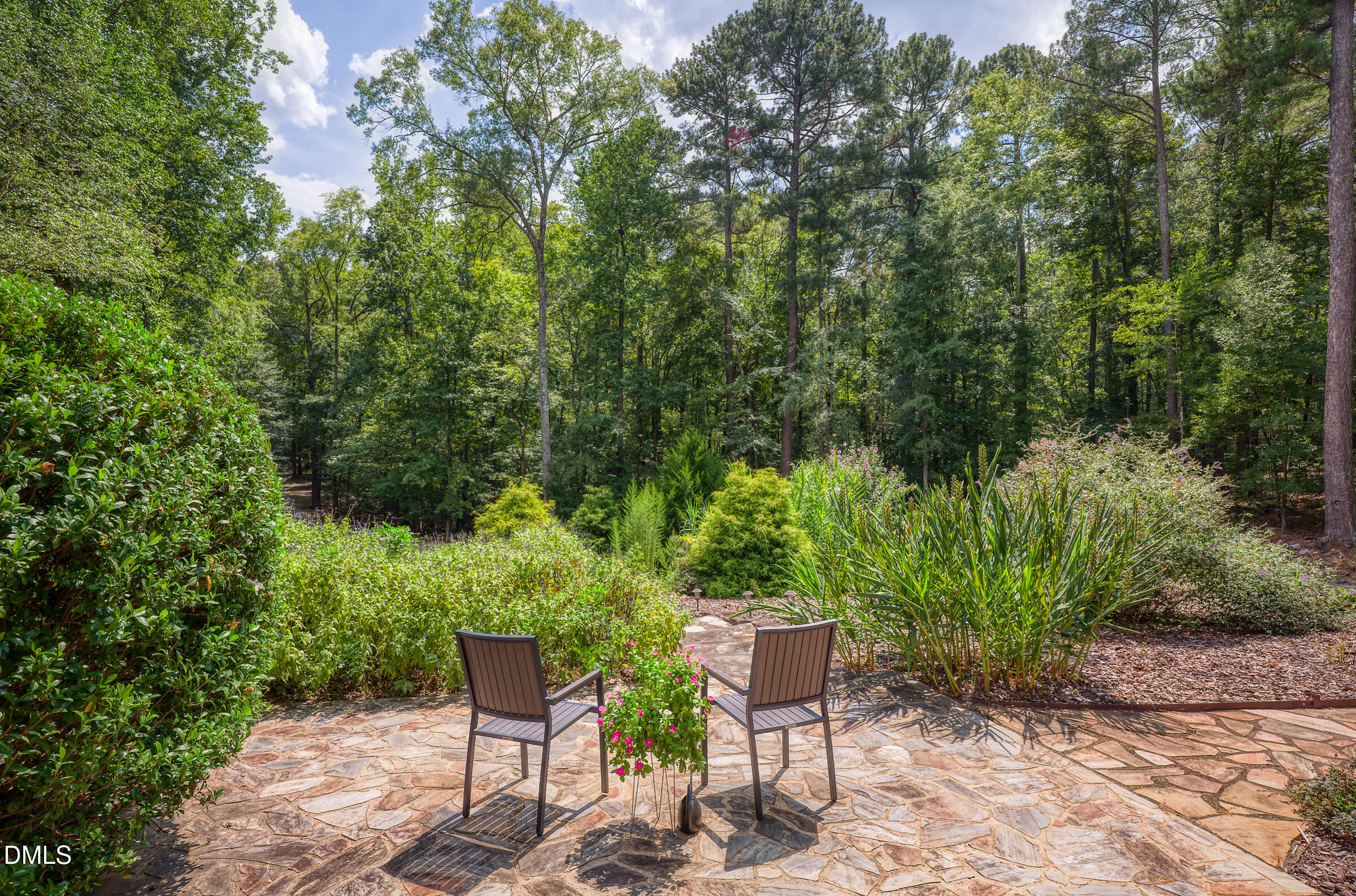 Flagstone patio with two chairs overlooks a lush, wooded garden.