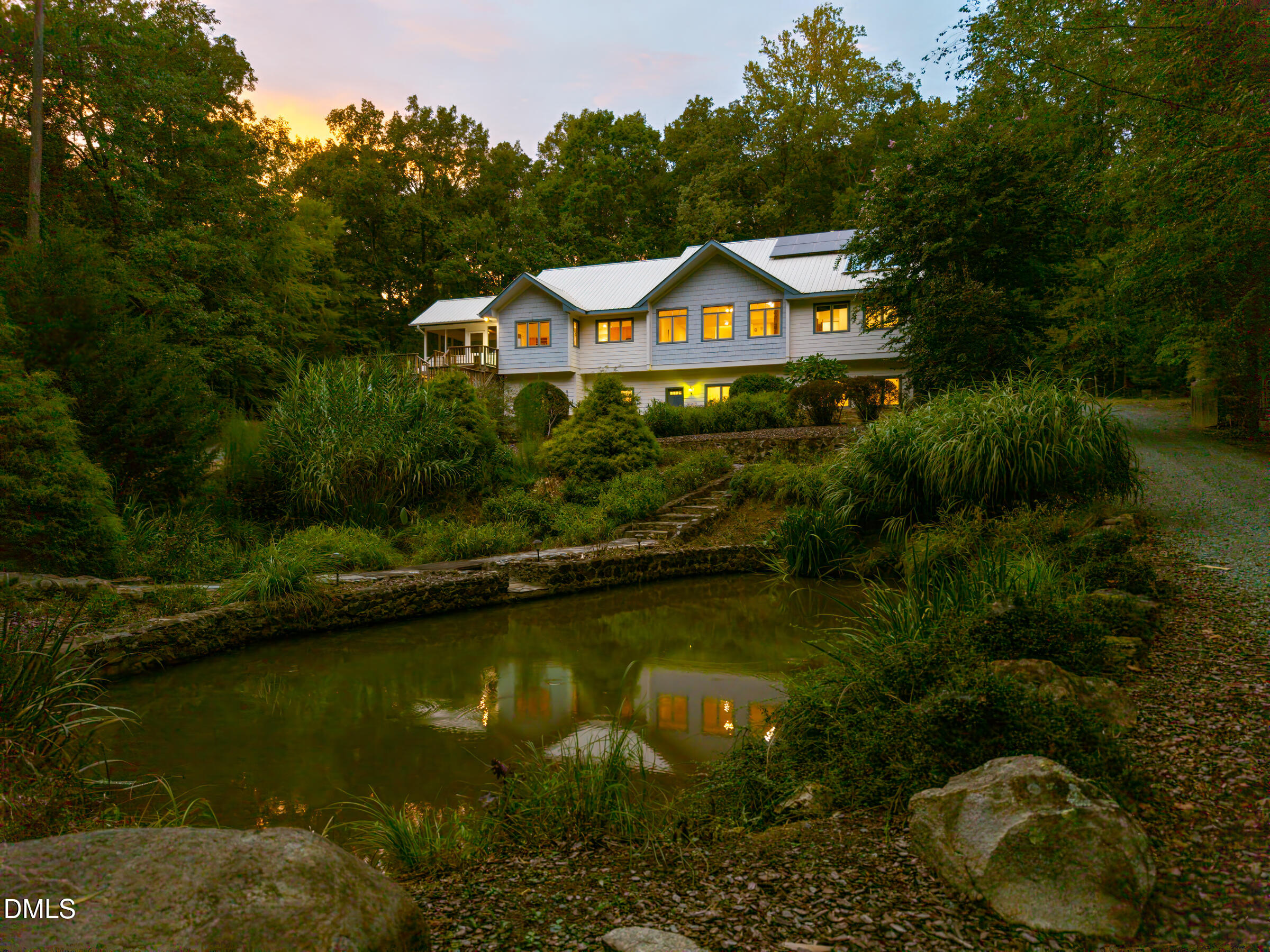 Wooded home at dusk, with lit windows reflected in a stone-edged pond.