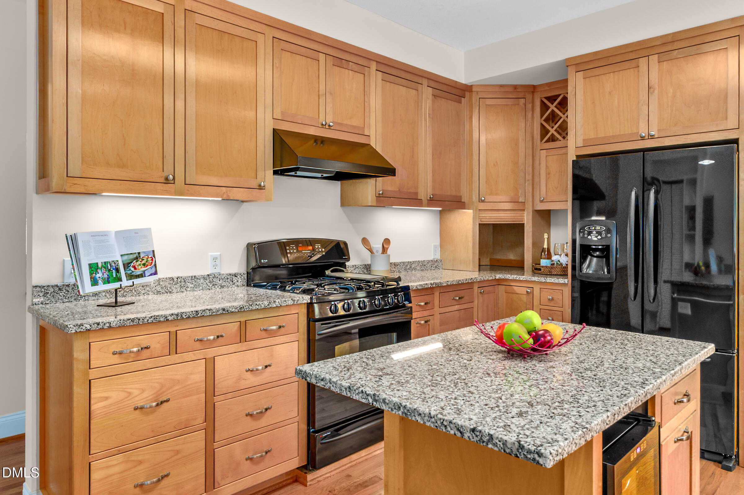 Kitchen with warm wood cabinets, granite island, gas range, and black refrigerator.