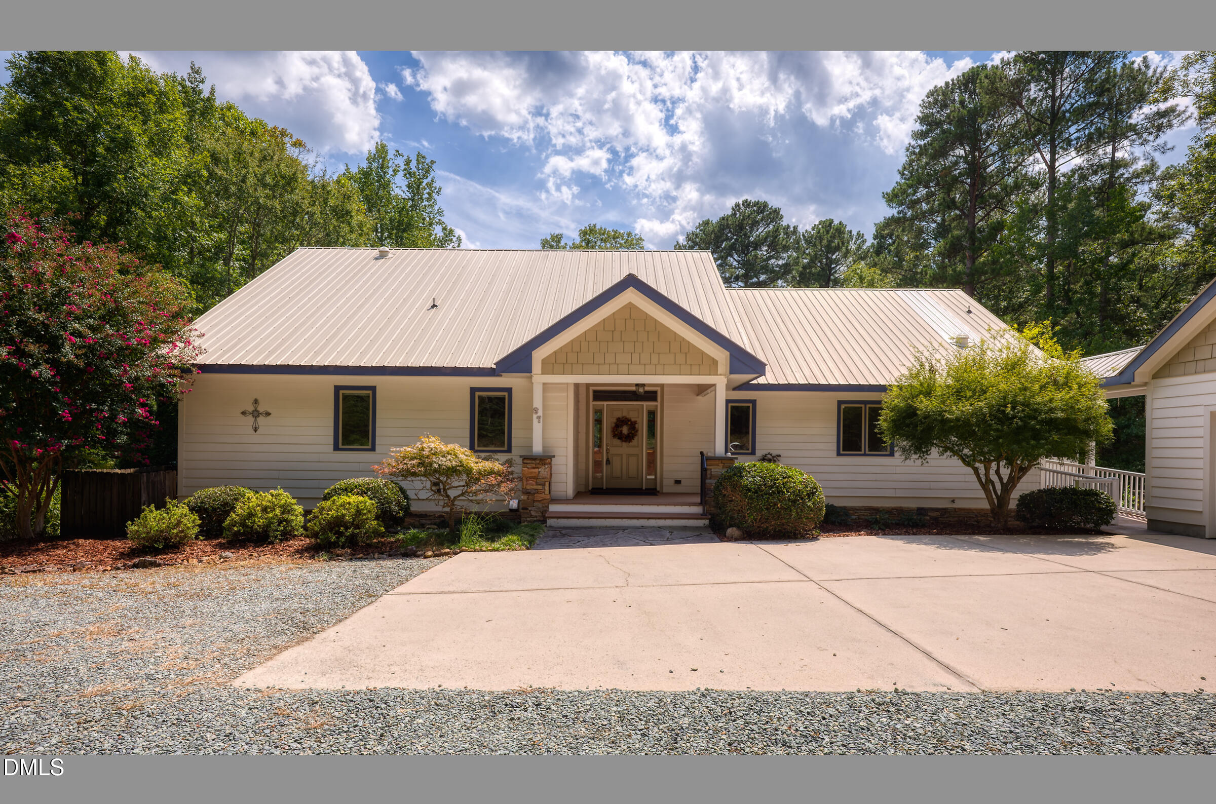 Single-story home with a pale metal roof, covered entry, landscaped shrubs, and a wide driveway.