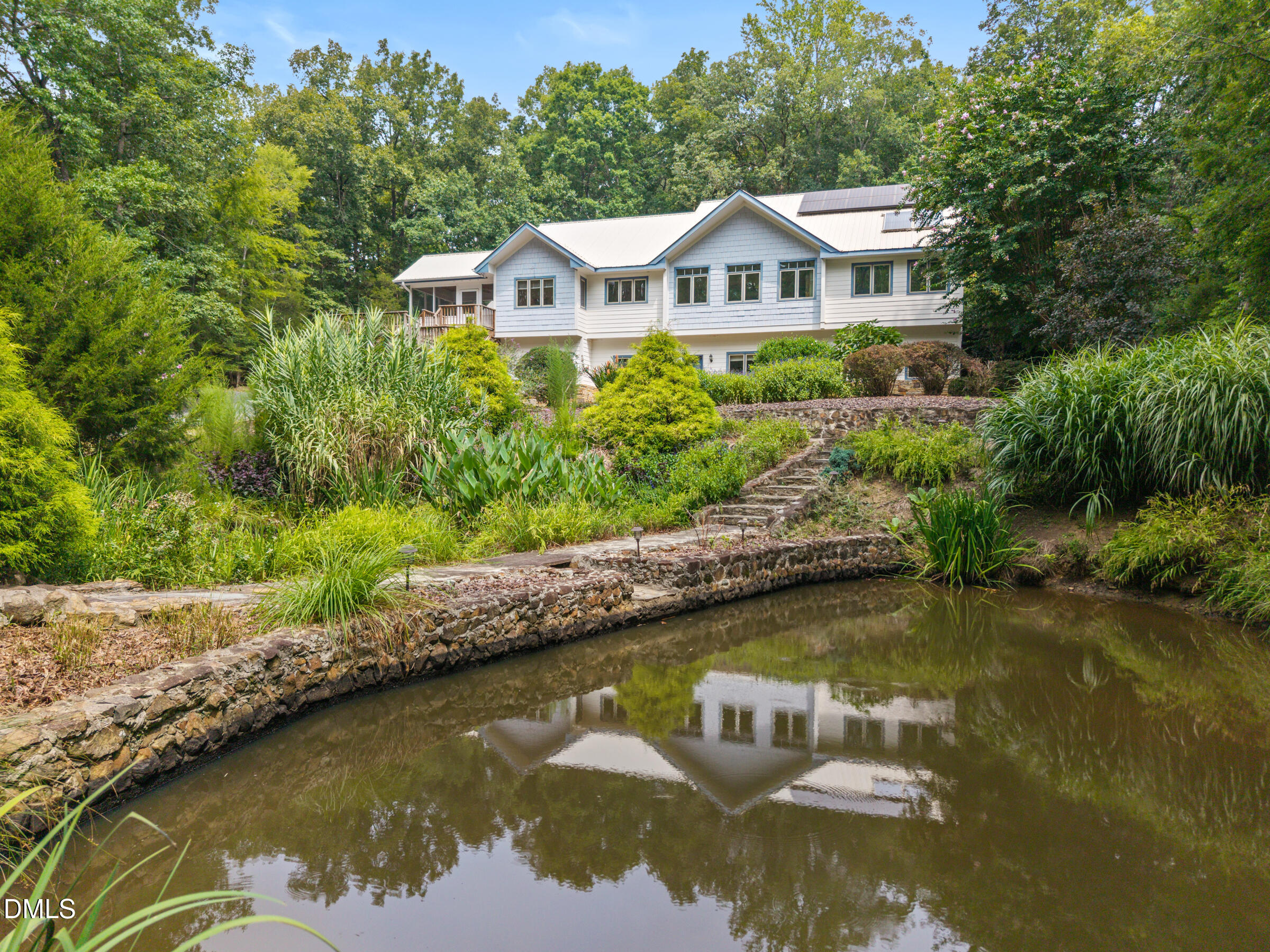 White house reflected in a landscaped pond, with stone walls and a garden path.