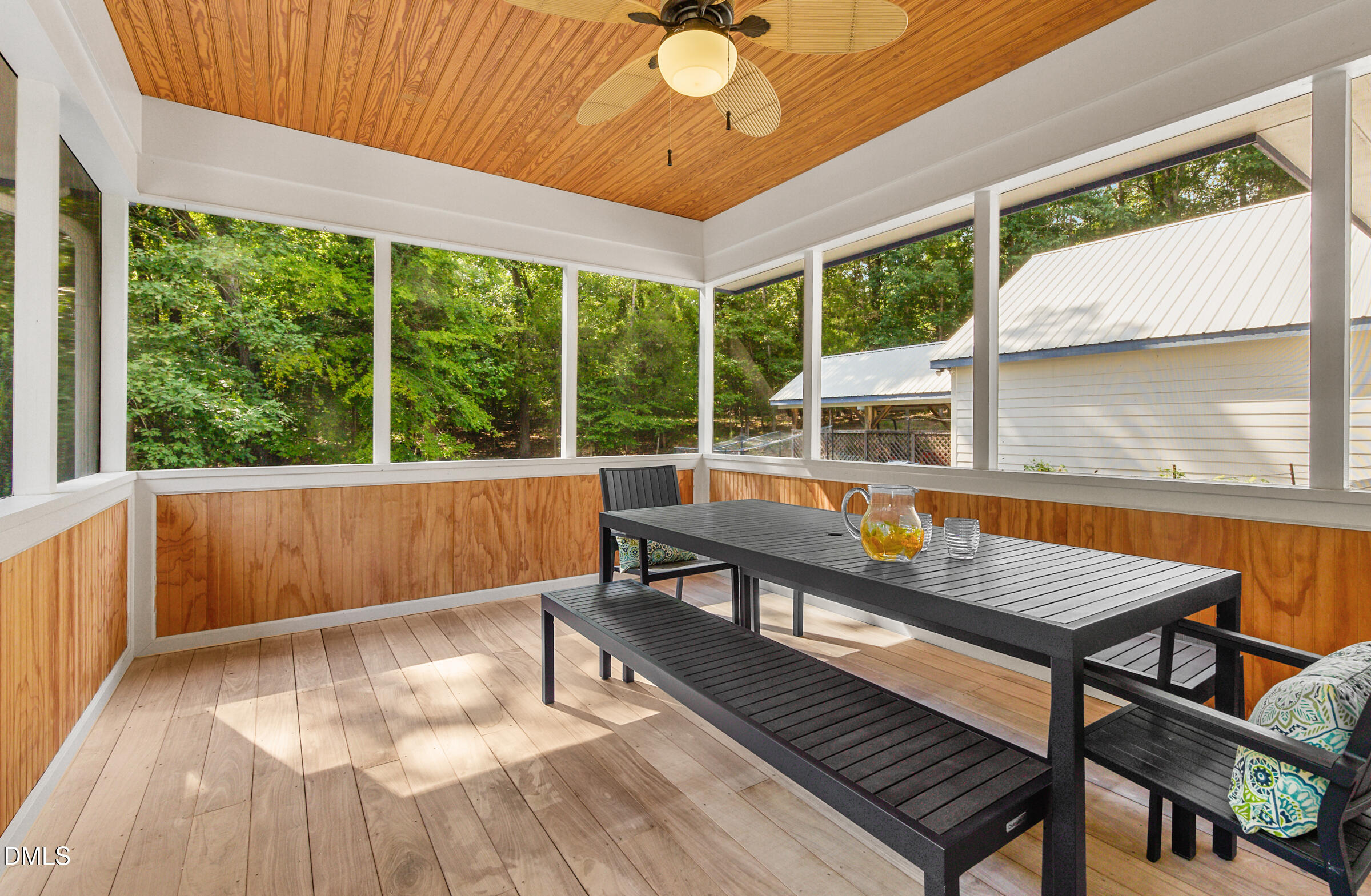 Screened porch with a wood-plank ceiling, black dining table, and views of leafy trees.
