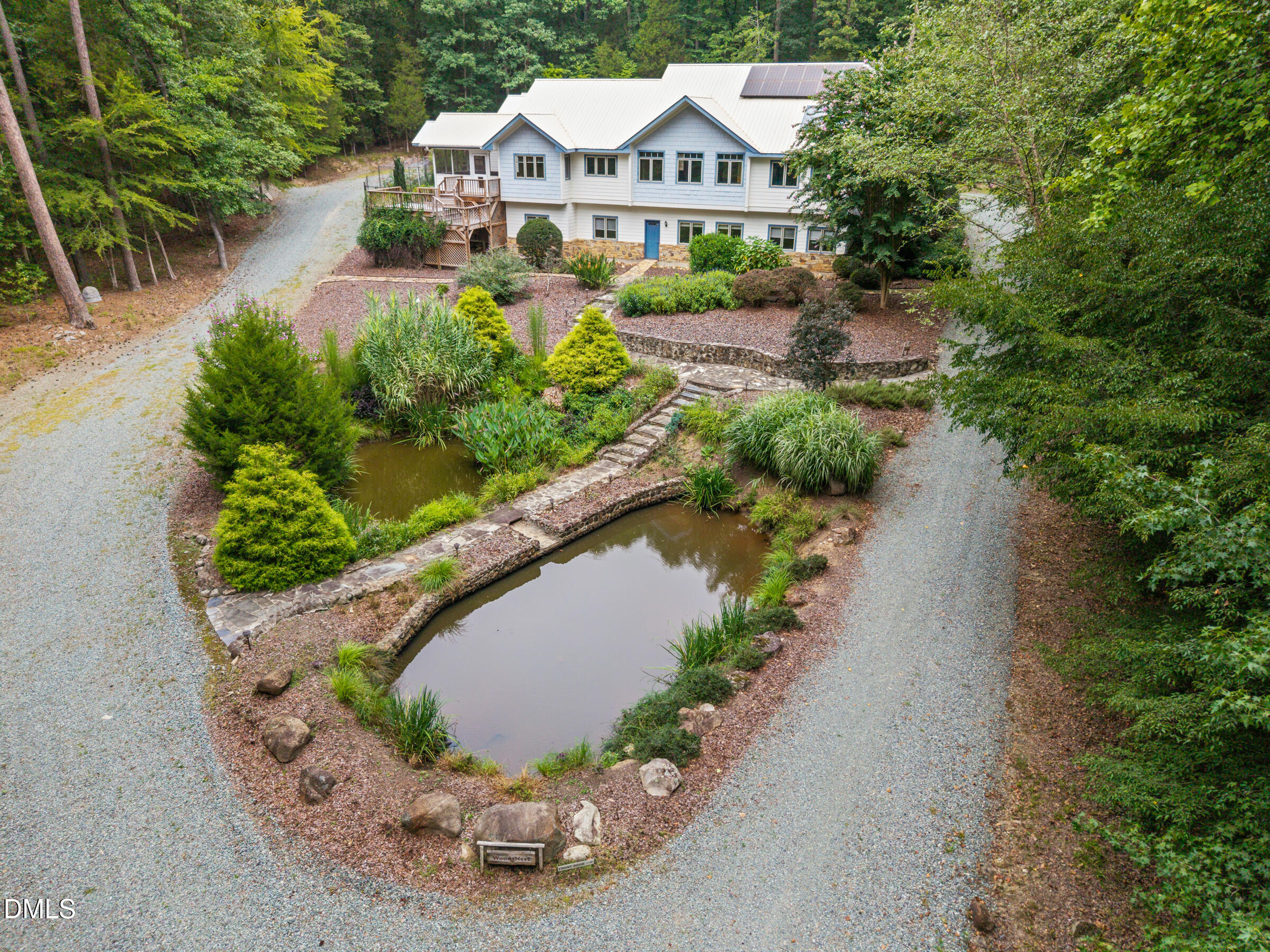 Aerial view of a white home with solar panels, landscaped ponds, stone paths, and gravel drives.
