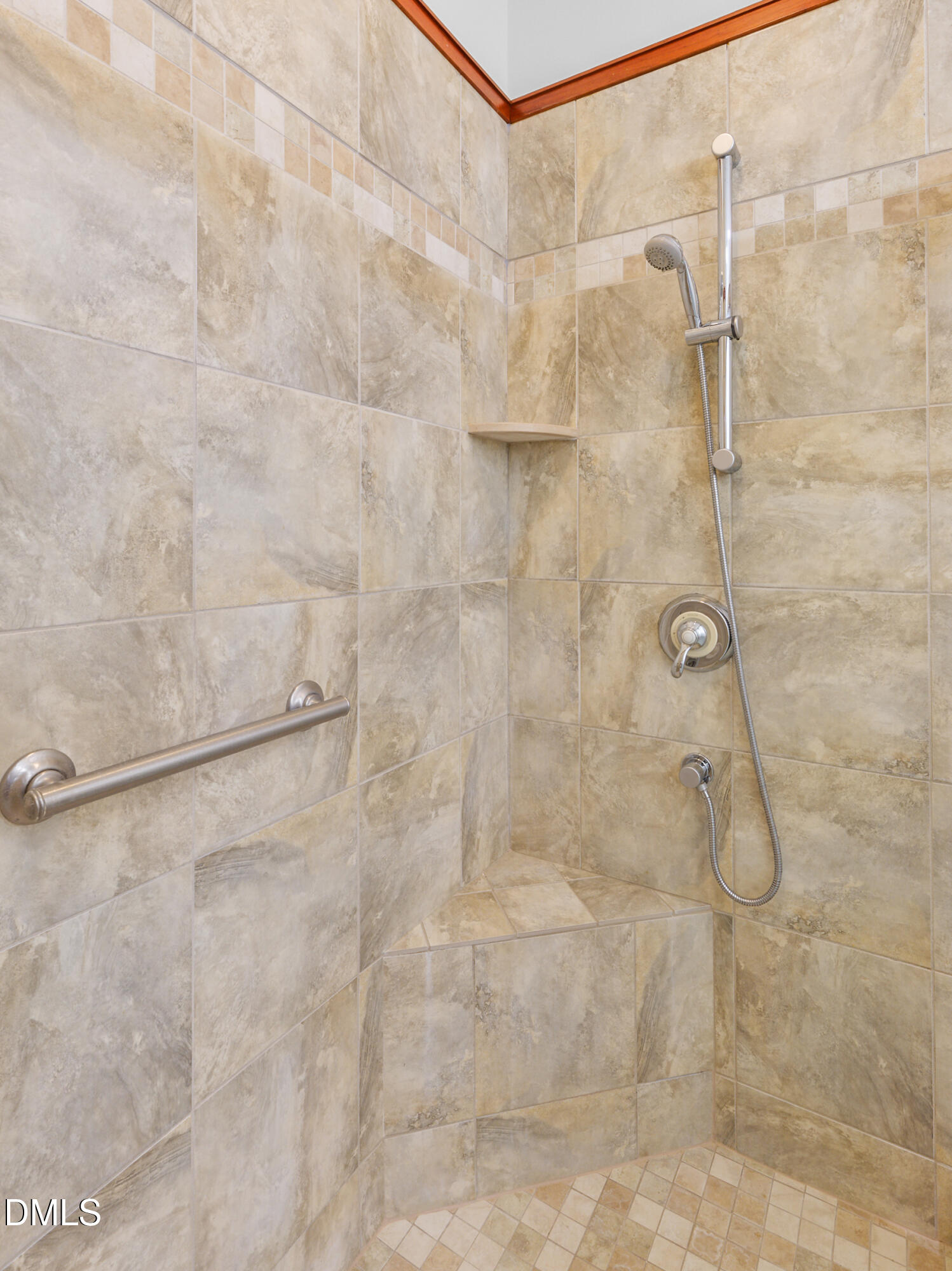 Tiled walk-in shower with a built-in corner seat, handheld showerhead, and stainless grab bar.