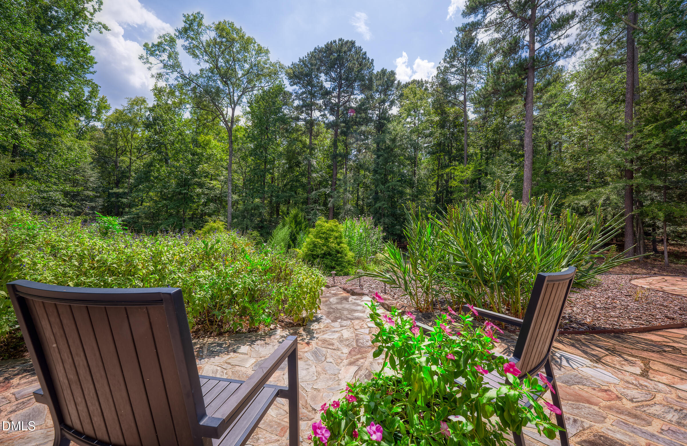 Flagstone patio with two chairs overlooking flowering plants and dense woods.