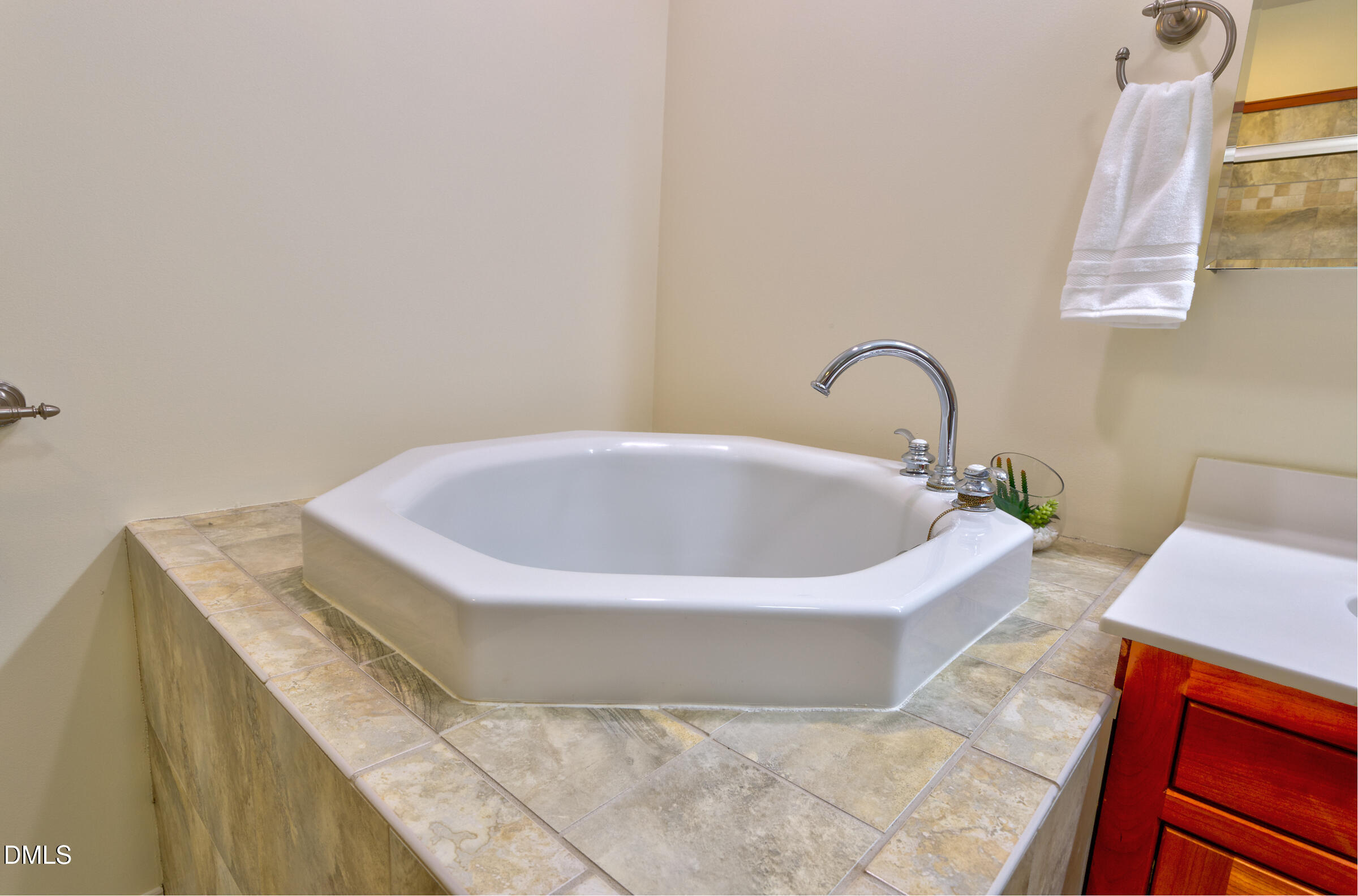 Corner soaking tub with chrome faucet set into a tiled platform beside a wood vanity.