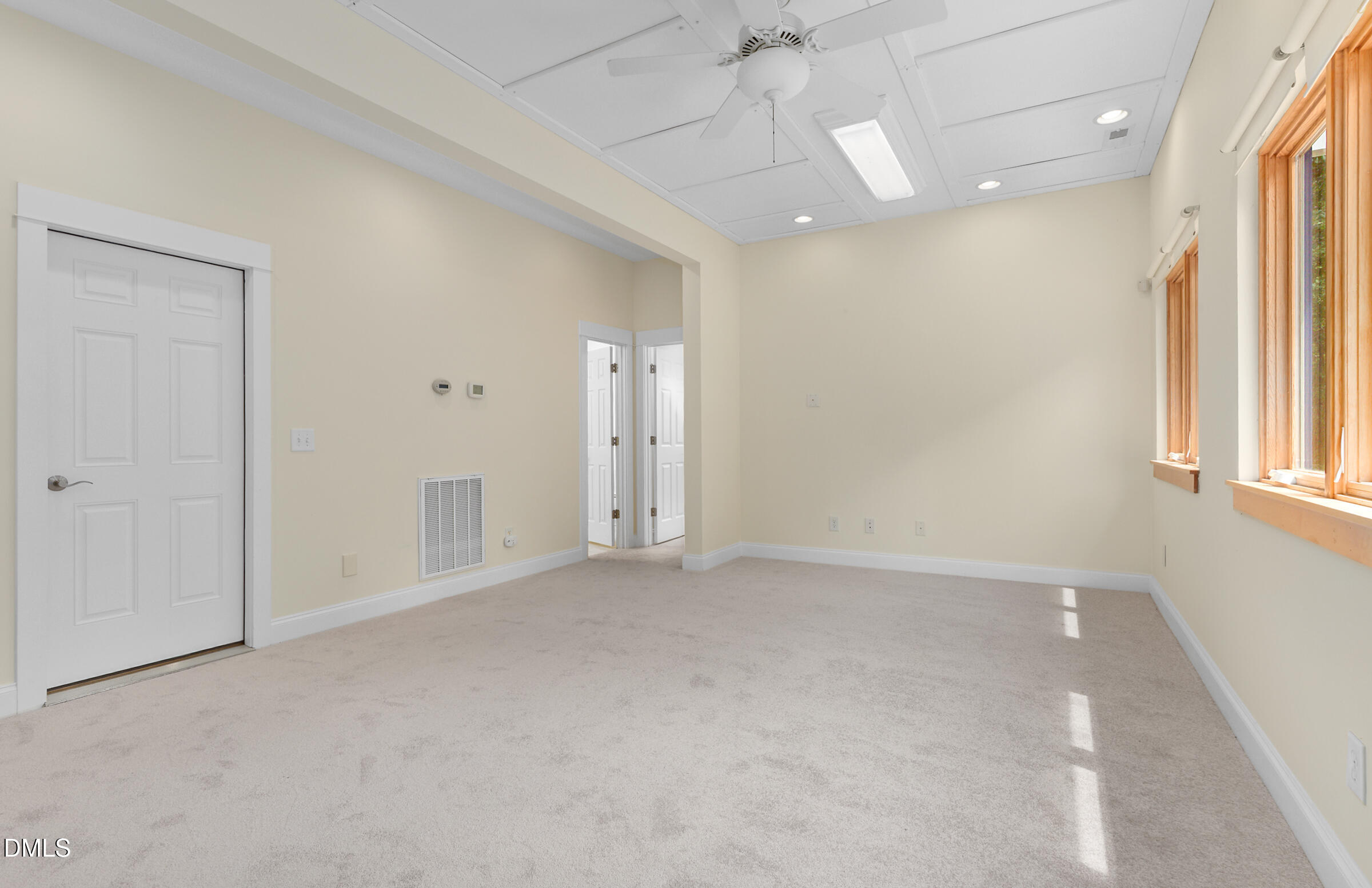 Empty carpeted room with a ceiling fan, recessed lights, and tall wood-trimmed windows.
