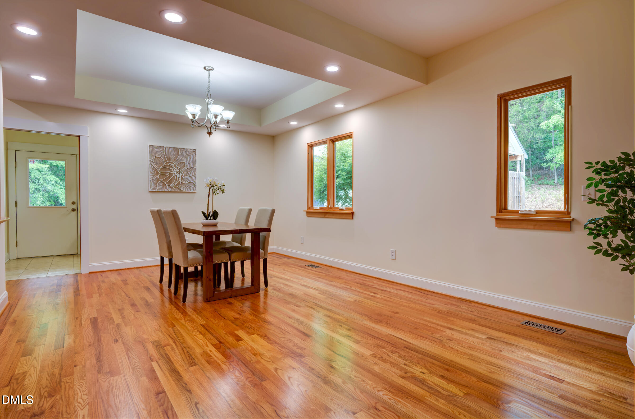 Dining room with a wood table, polished hardwood floors, tray ceiling, and large windows.