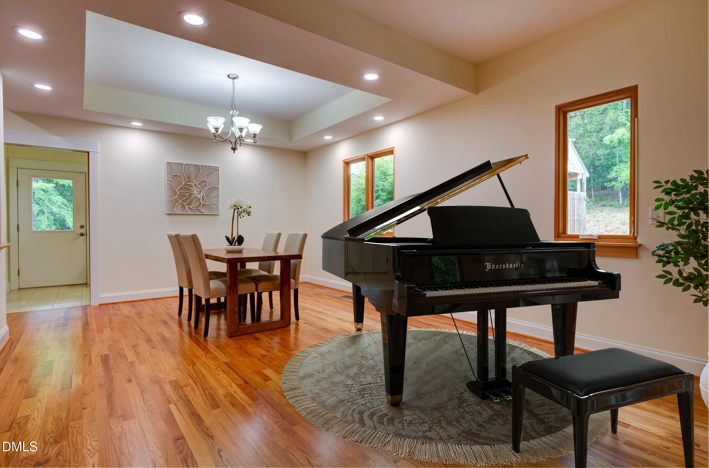 Dining room with a black grand piano, round rug, wooden table, and hardwood floors.