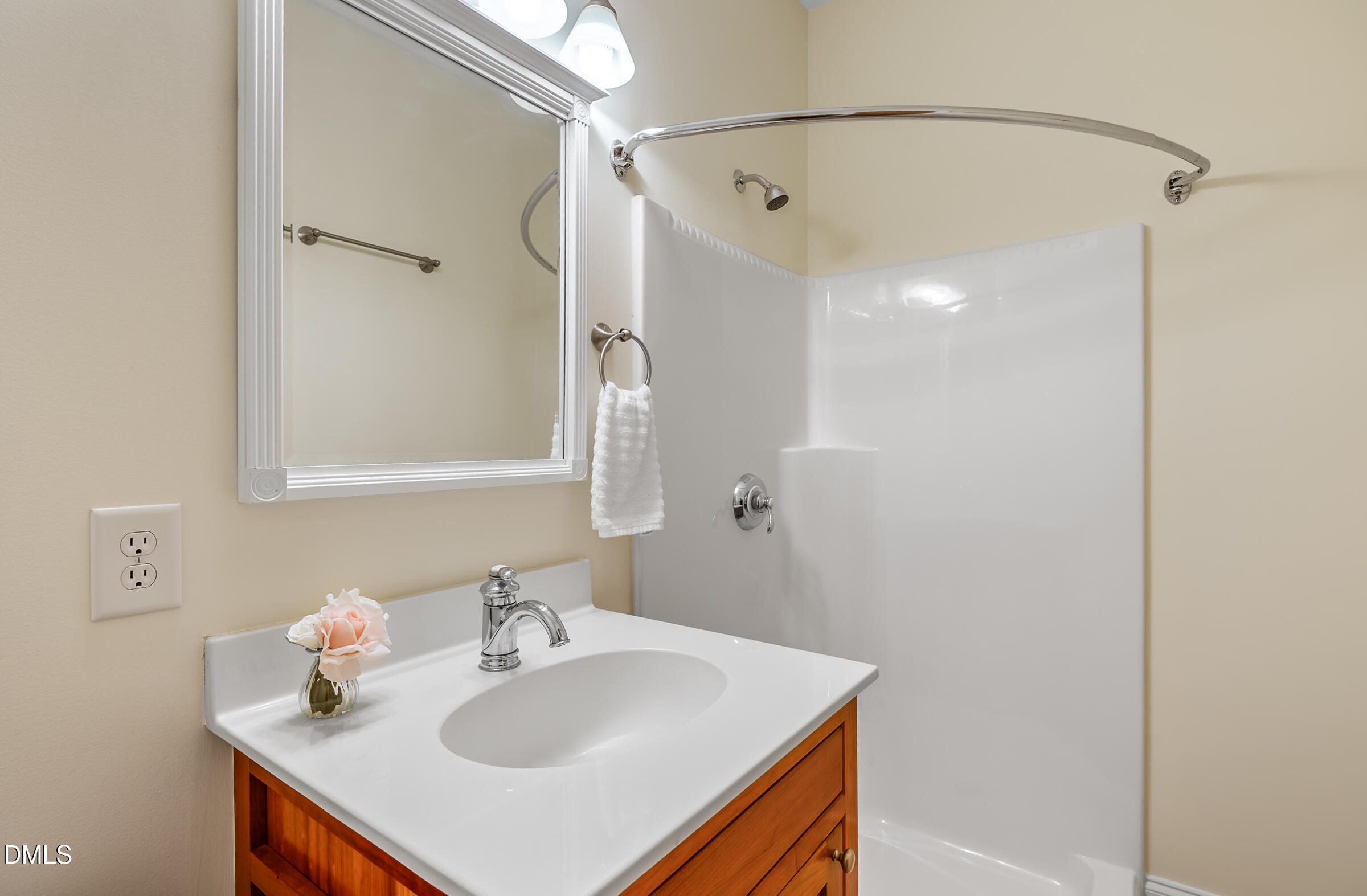 Bathroom vanity with a white sink and wood cabinetry beside a white shower enclosure.