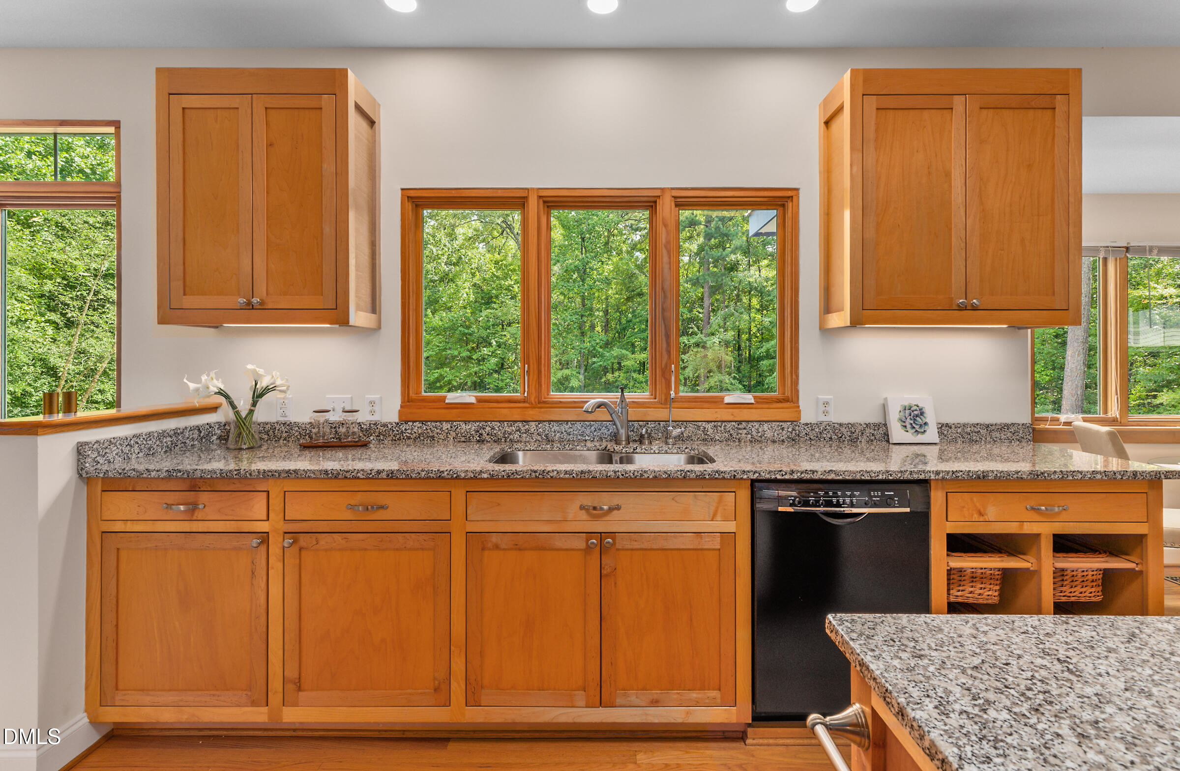 Kitchen with warm wood cabinets, granite counters, and a sink facing windows overlooking trees.
