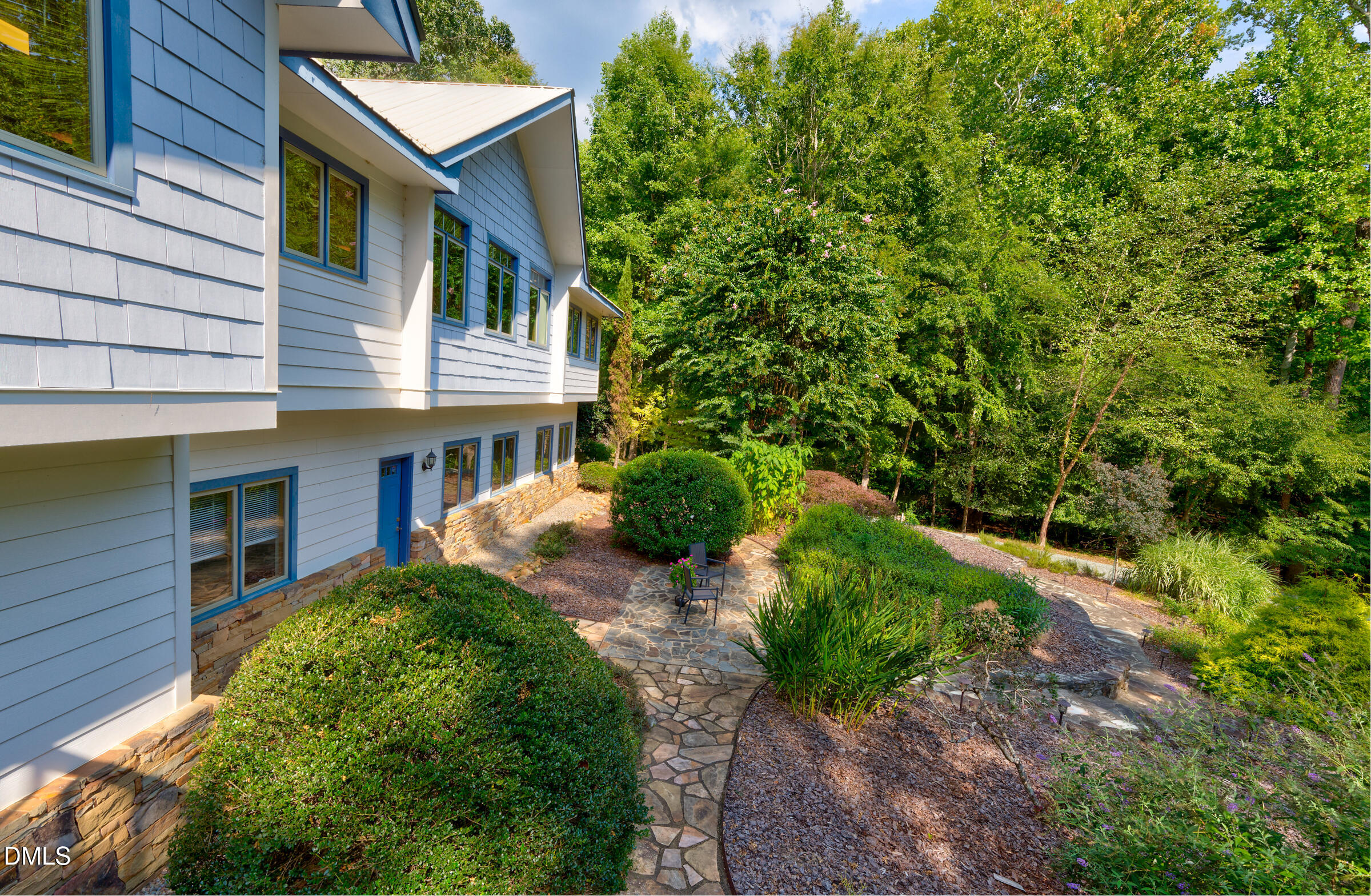 Light blue home beside a landscaped flagstone path and patio, surrounded by mature trees.