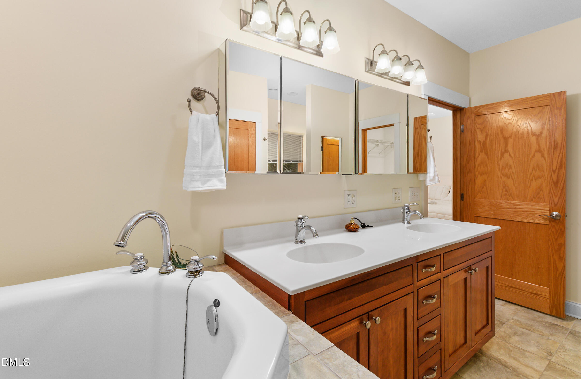 Bathroom with a soaking tub and double-sink wood vanity beneath mirrored cabinets.
