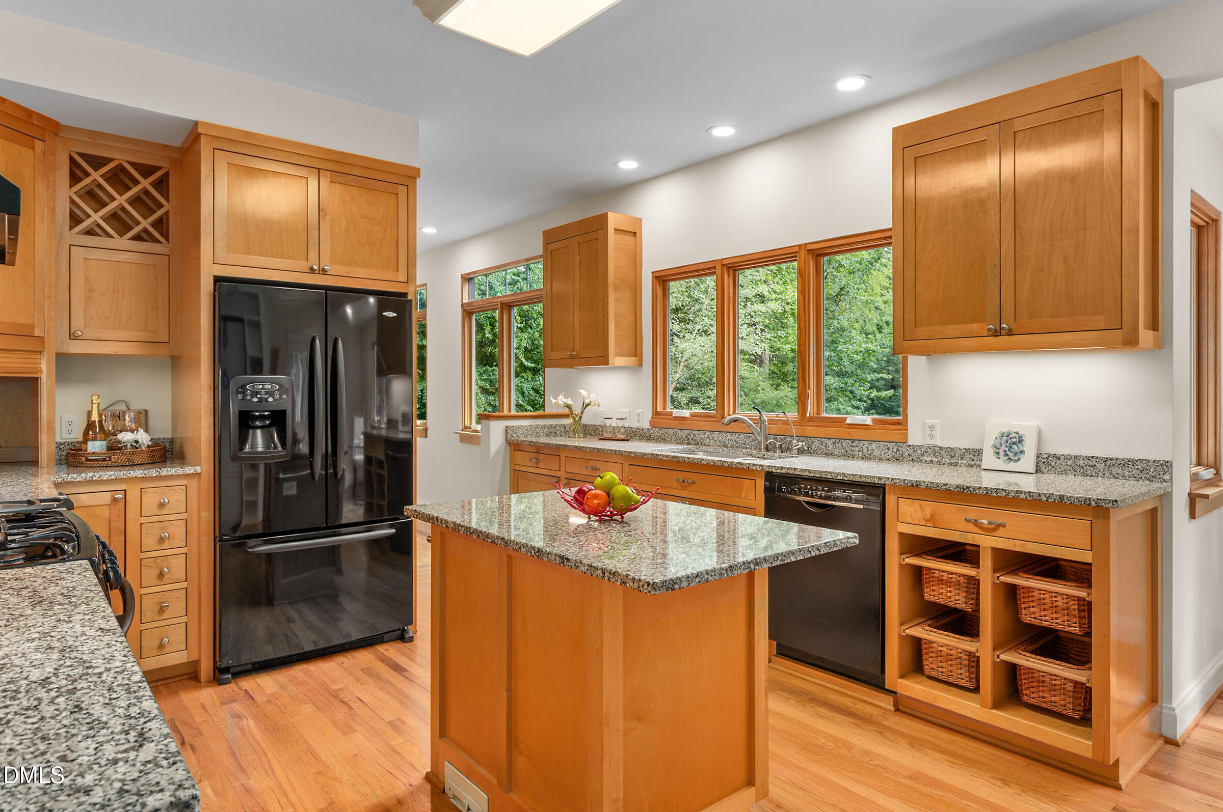 Kitchen with a granite-topped island, warm wood cabinetry, and large windows overlooking trees.