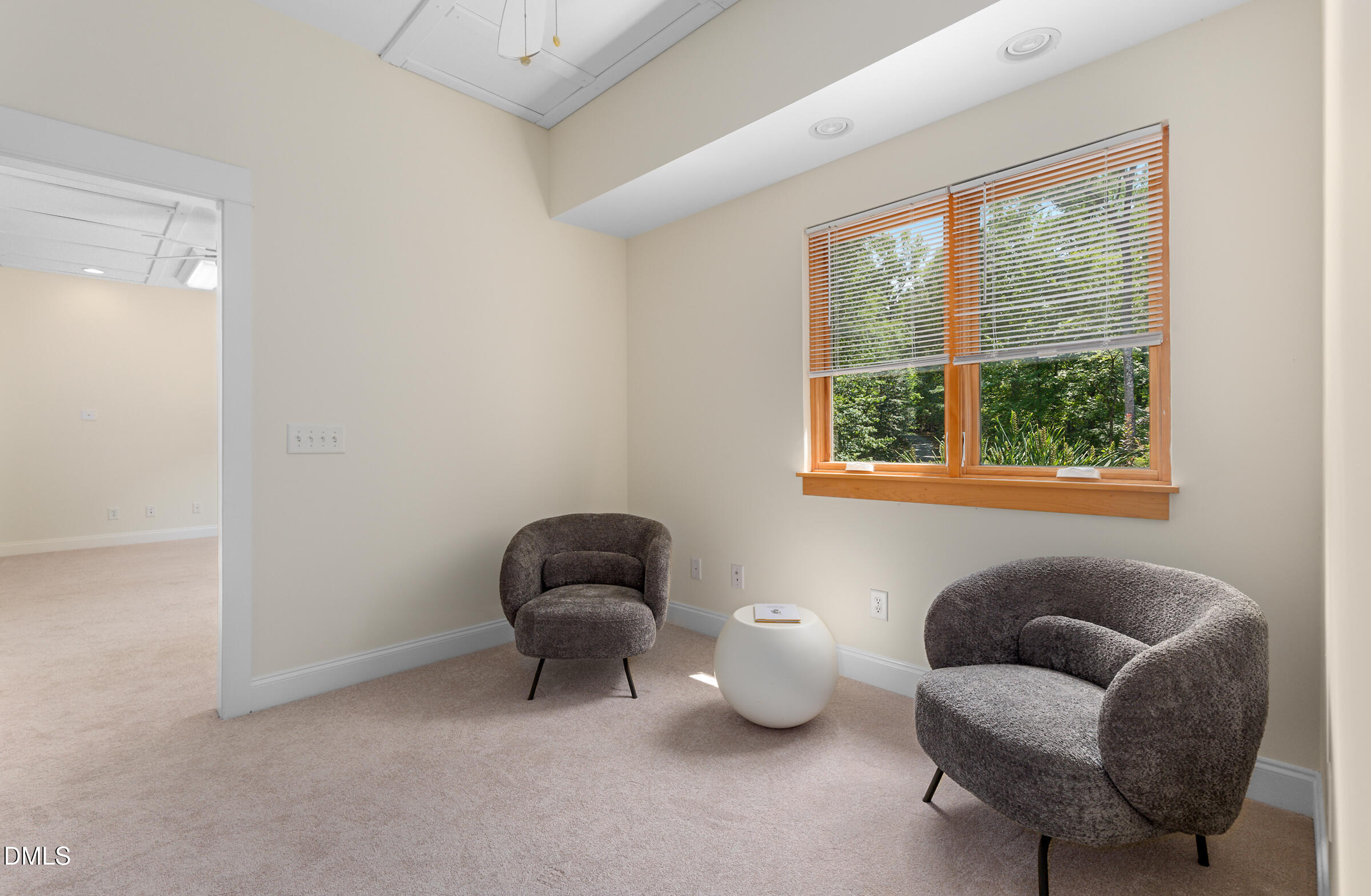 Sitting area with two charcoal chairs beside a large wood-trimmed window overlooking greenery.