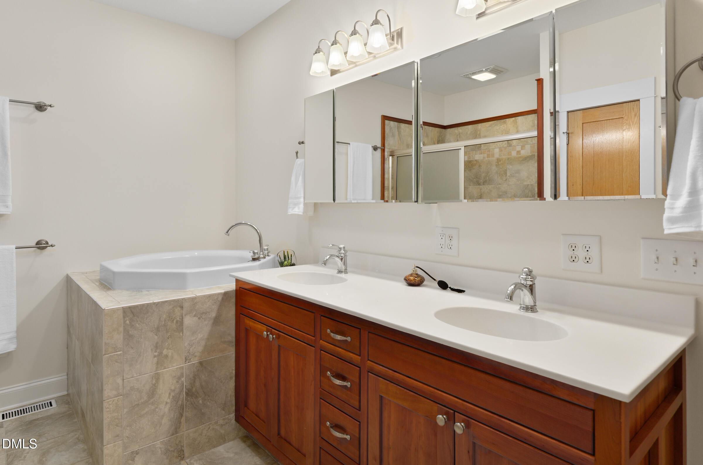 Bathroom with a tiled corner soaking tub and a reddish-brown double vanity beneath mirrored cabinets.