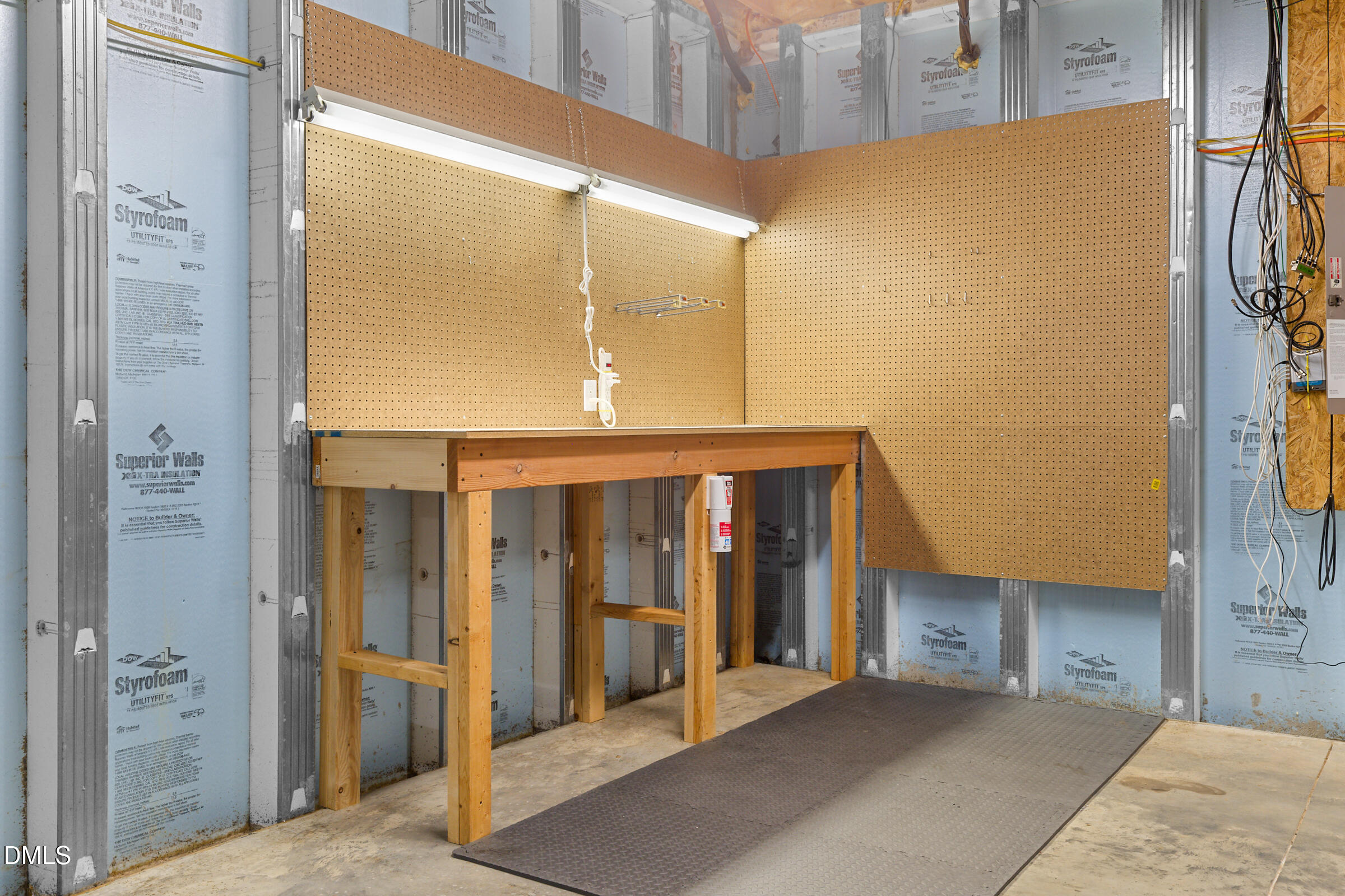 Unfinished garage workshop with a wooden workbench, pegboard walls, and exposed insulation.