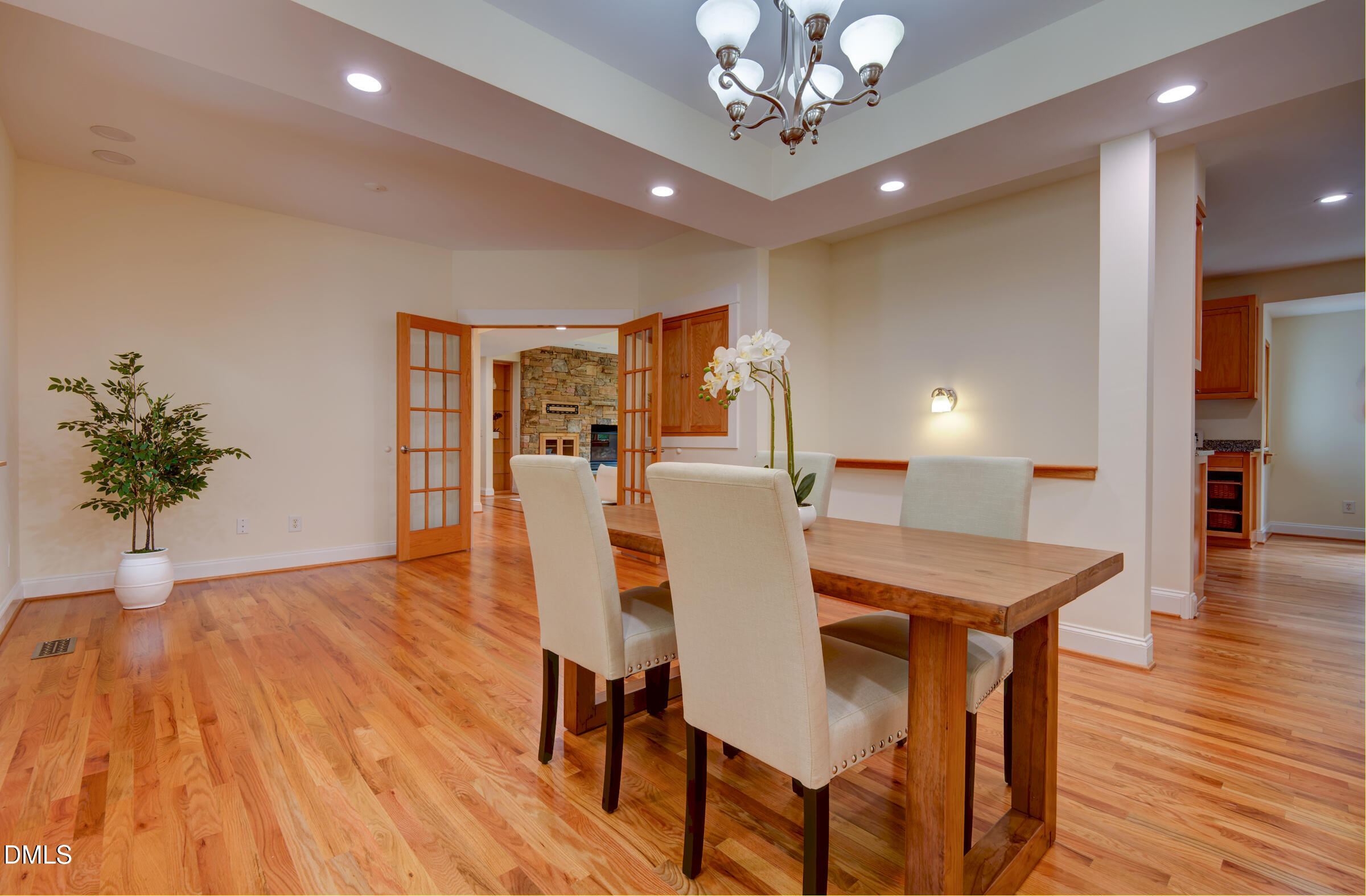 Dining room with a wood table, cream chairs, hardwood floors, and French doors opening toward a stone fireplace.