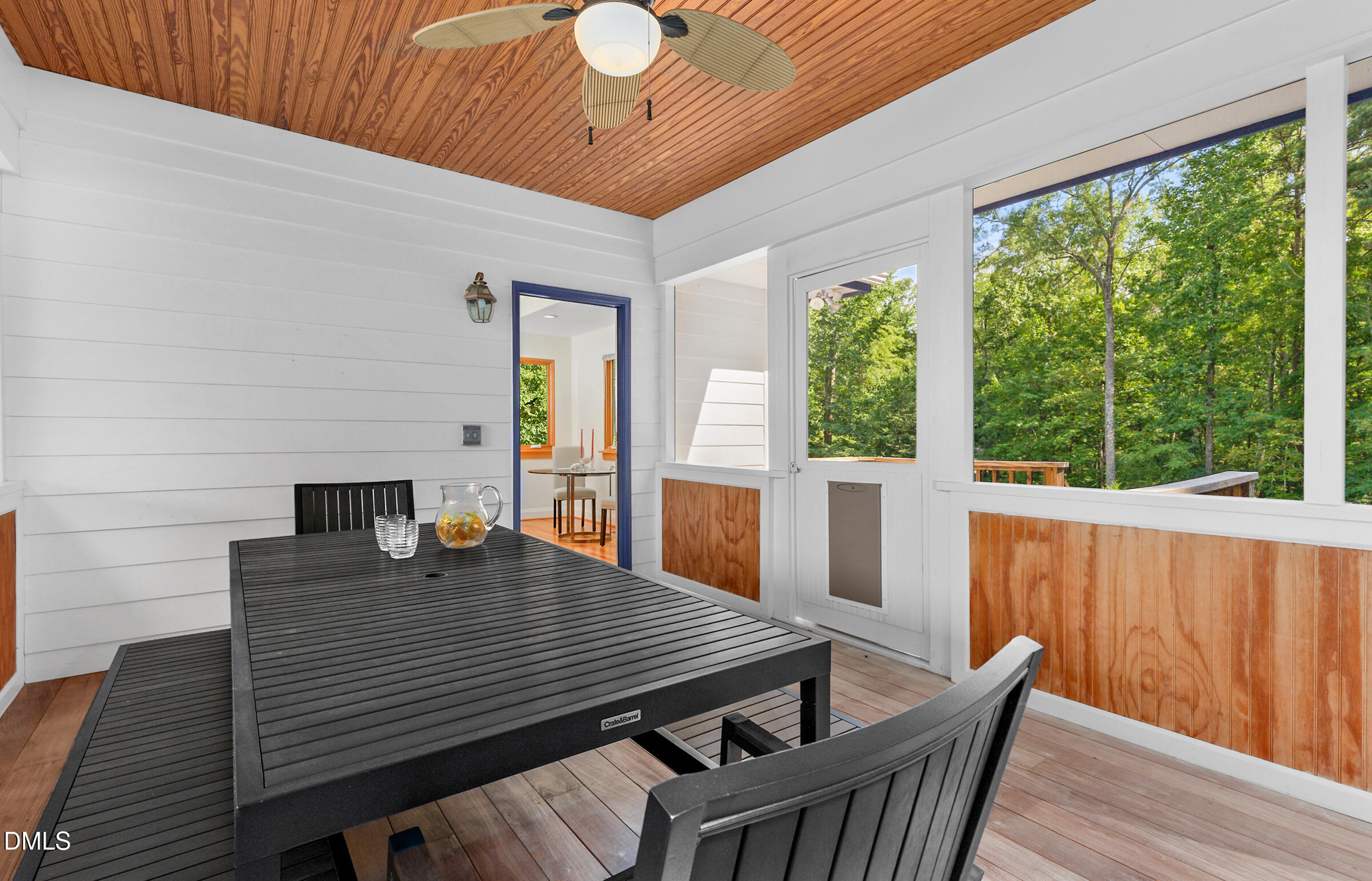 Screened porch with black dining furniture, a wood-plank ceiling, and views of leafy trees.