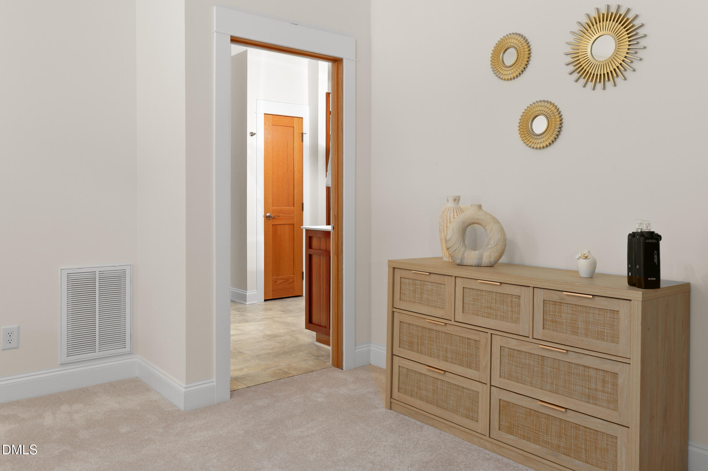 Bedroom with a woven-front dresser, gold sunburst mirrors, and an open doorway to a tiled area.