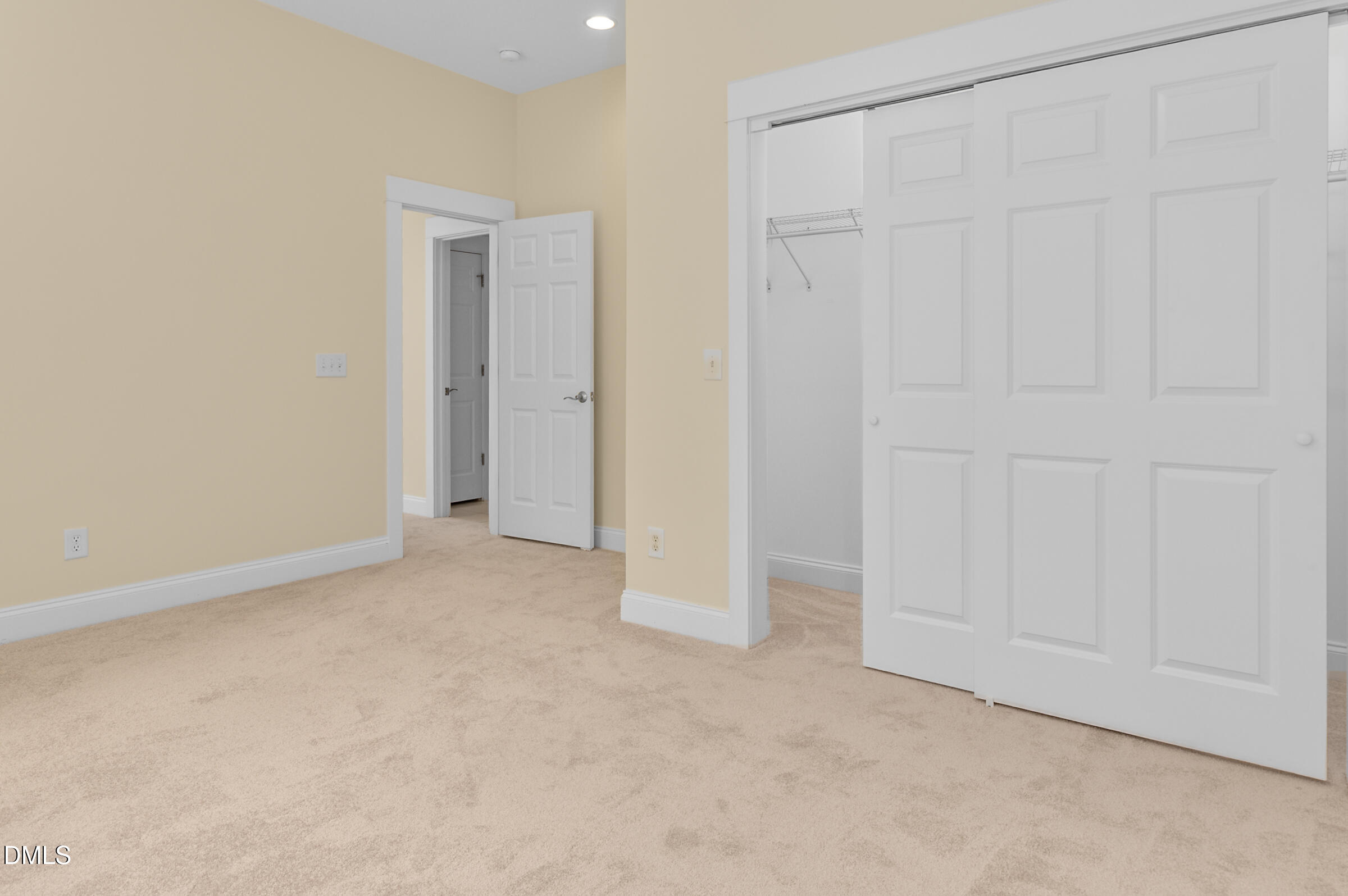 Vacant carpeted room with pale yellow walls and a large white sliding-door closet.